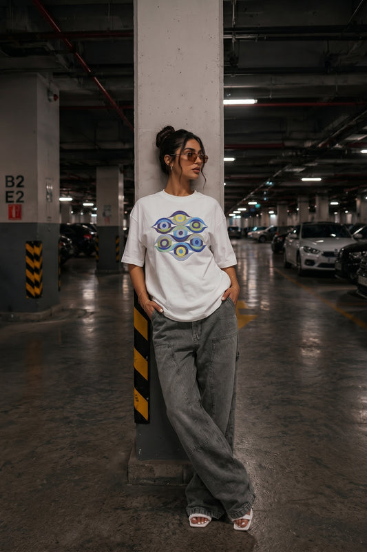 Person wearing a white t-shirt with a colorful embroidery design and gray pants in a parking garage.