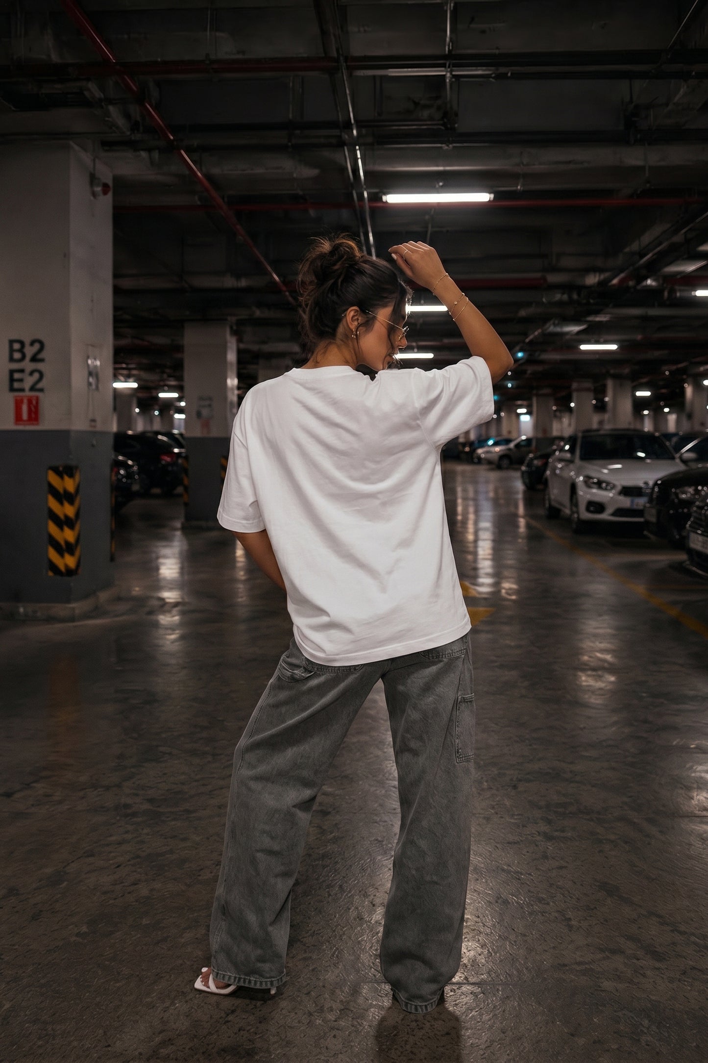 Person in a white shirt and gray pants standing in a dimly lit parking garage.