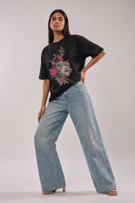 Woman wearing a black t-shirt with floral and butterfly embroidery design and blue jeans on a white background