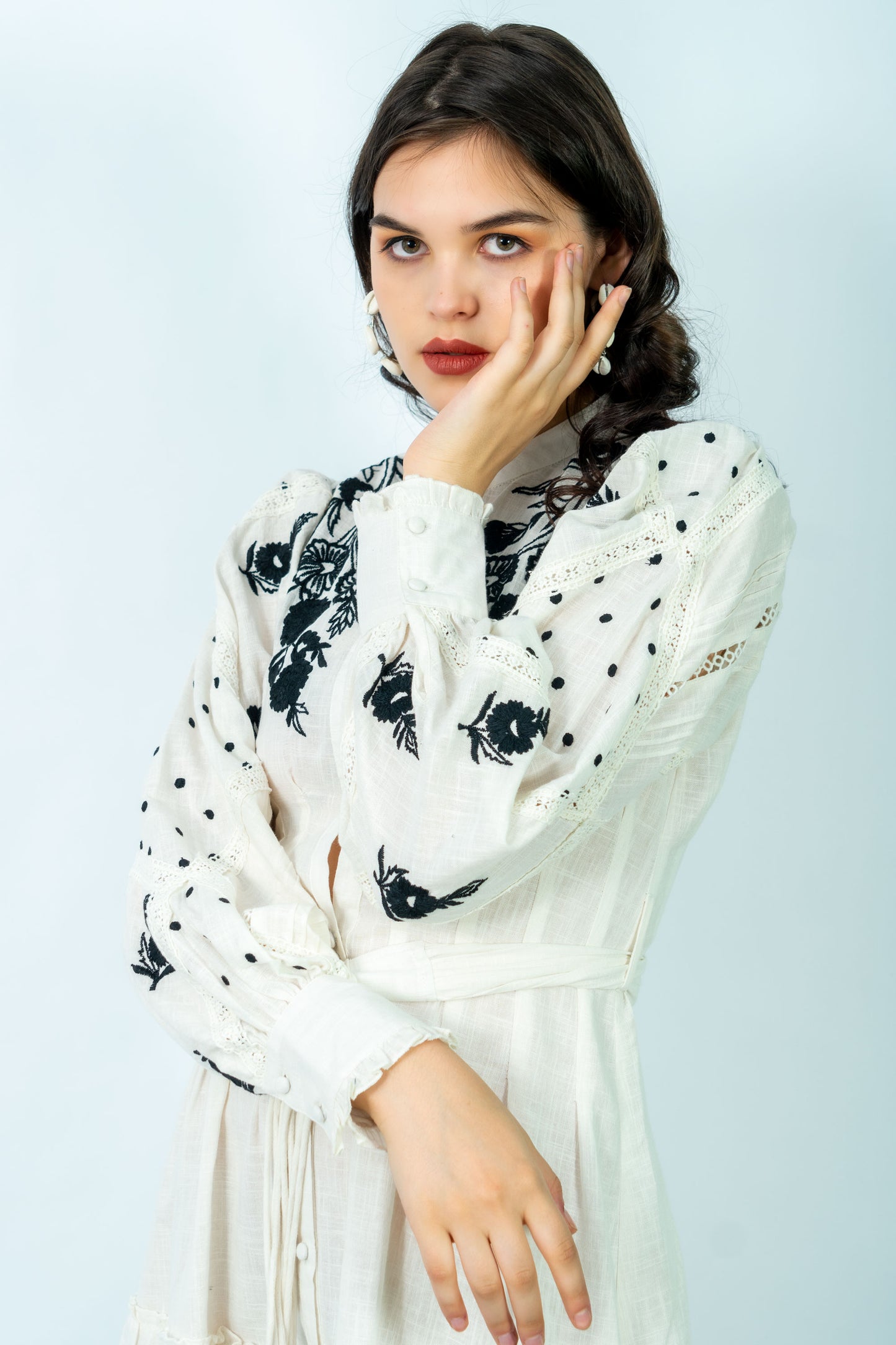 Woman wearing a white dress with black floral patterns against a light blue background
