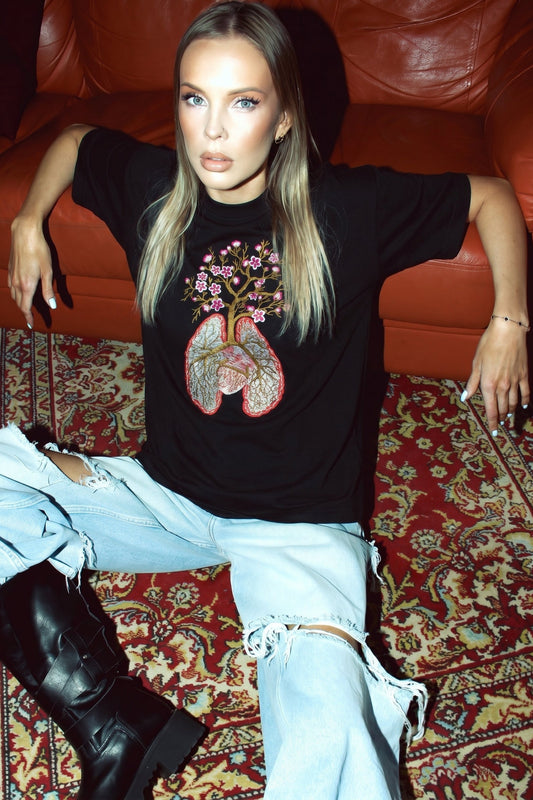 Woman wearing a black t-shirt with a graphic design, sitting on a red leather couch.