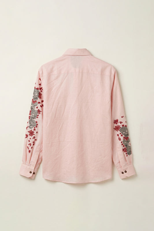 Pink shirt with floral and skull embroidery on a light beige background
