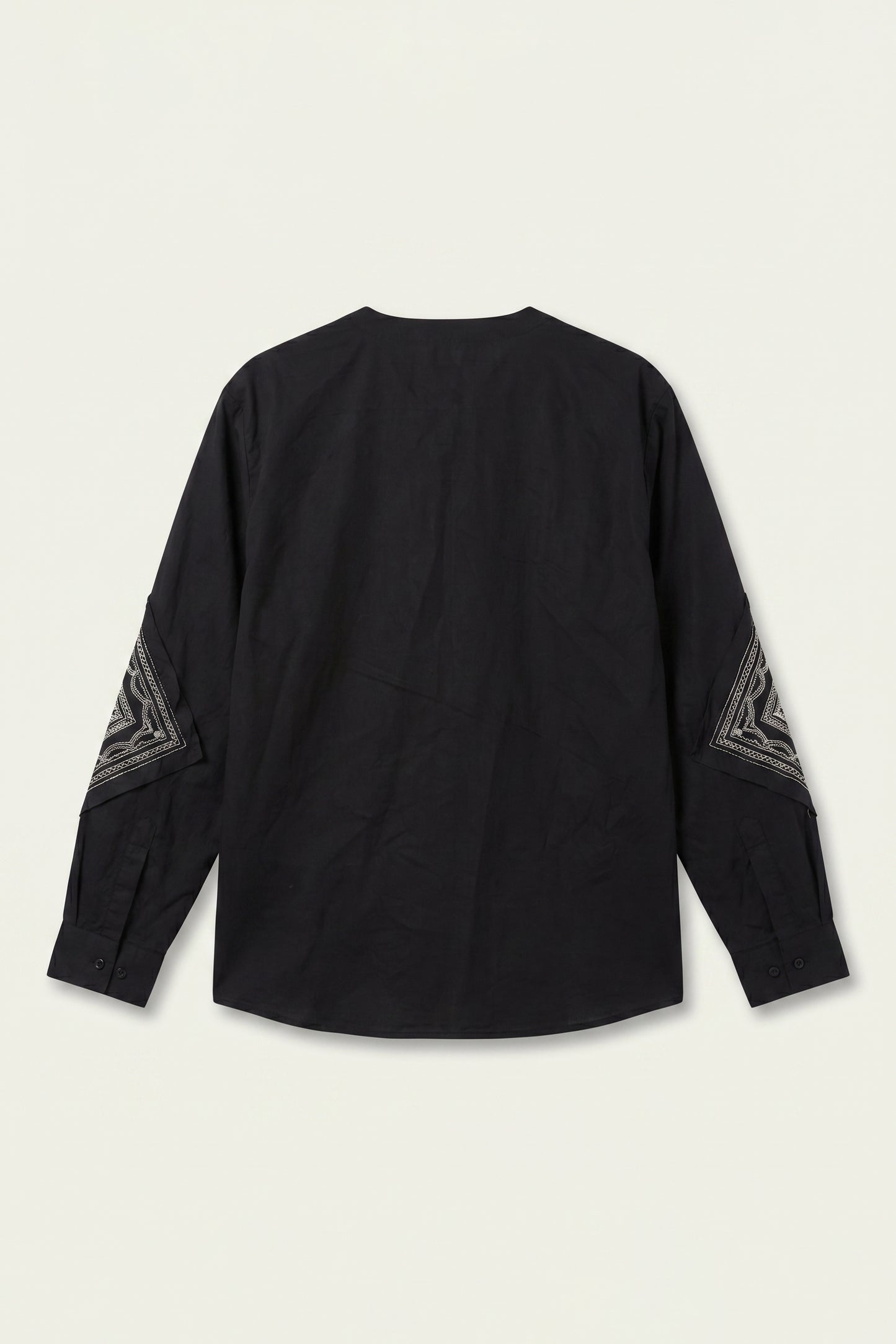 Black long-sleeve top with geometric patterns on sleeves against a beige background