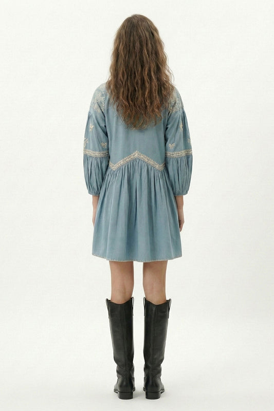 Model wearing a light blue dress with embroidery and black boots on a white background