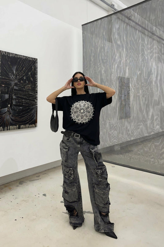 Person wearing a black t-shirt with a white design and gray pants in an art gallery.