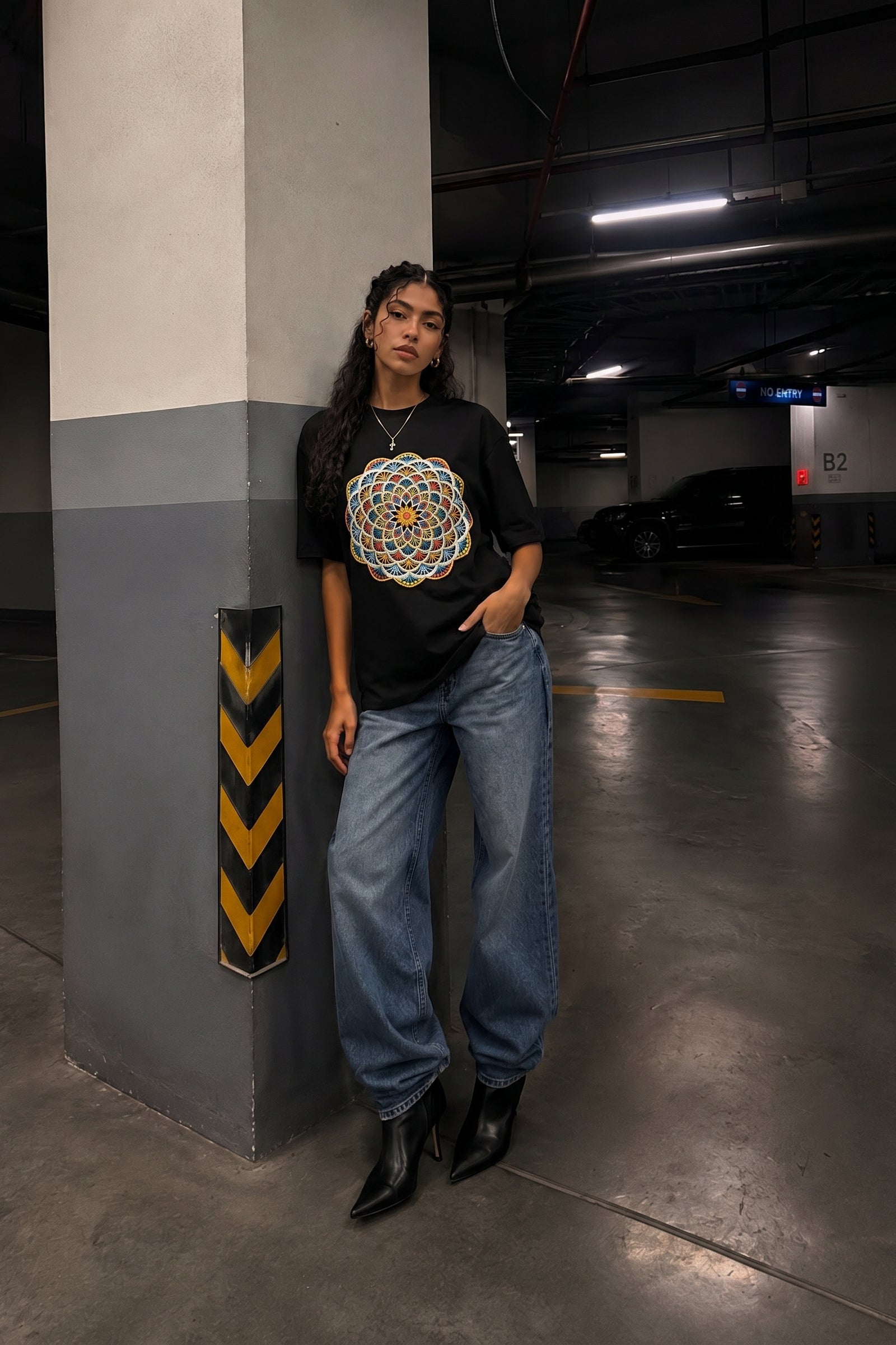Woman wearing a black t-shirt with a colorful embroidery design and blue jeans standing in a parking garage.