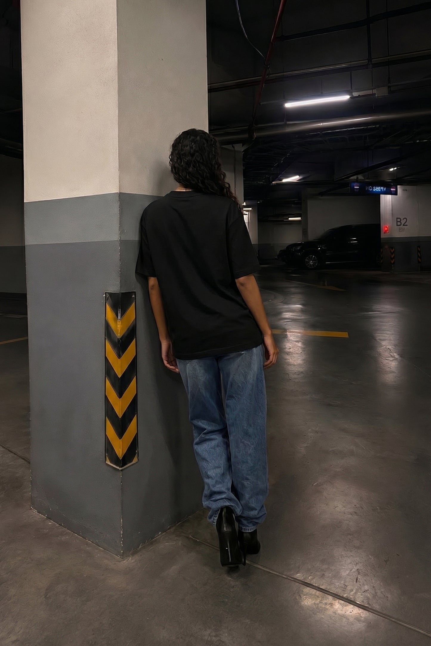 Person leaning against a column in a dimly lit parking garage