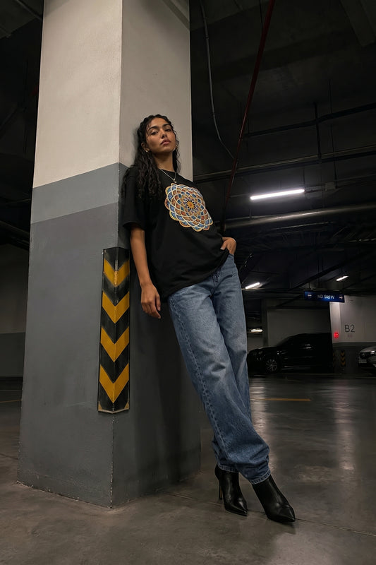 Person wearing a black t-shirt with a colorful embroidery design and blue jeans standing in a parking garage.