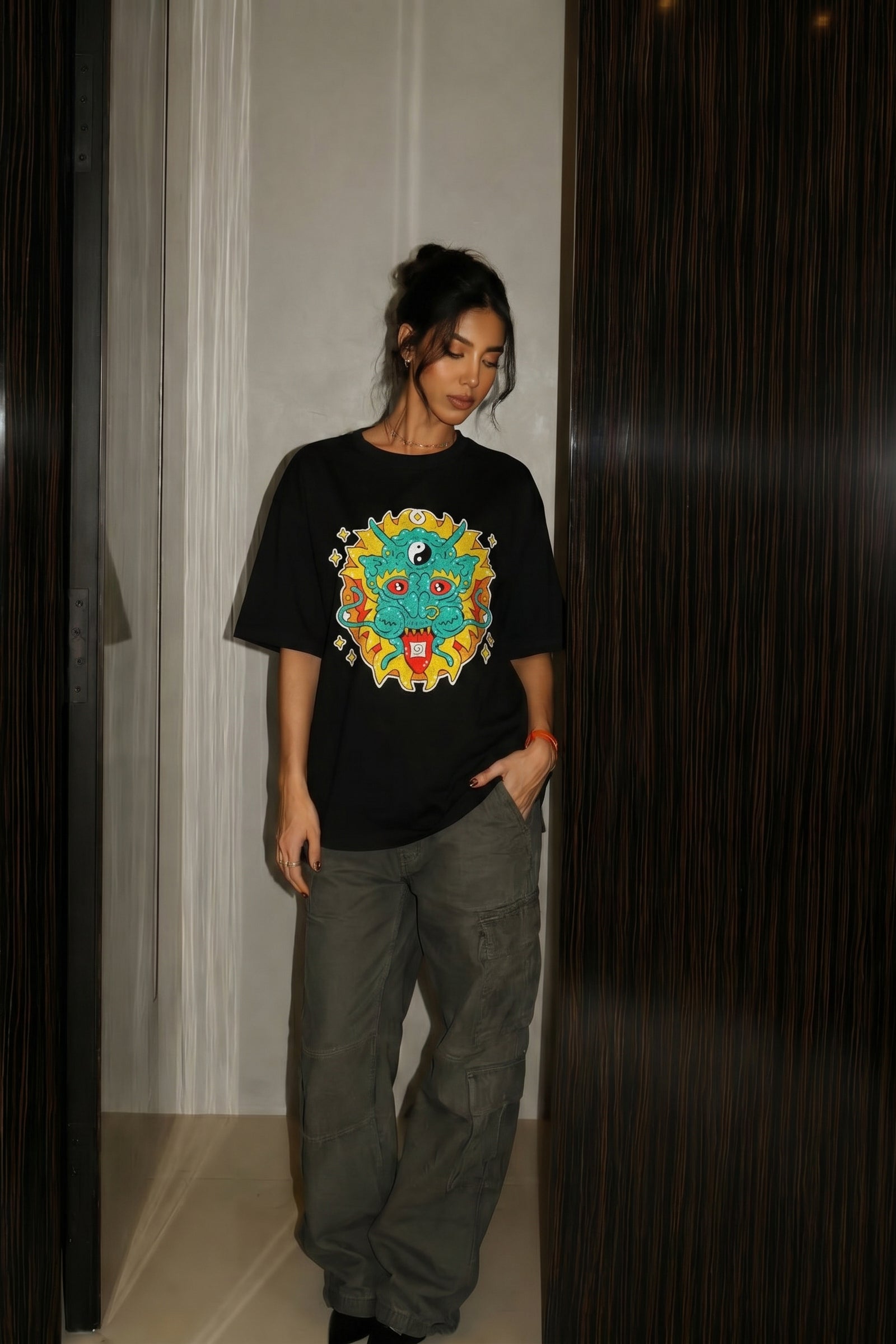 Person wearing a black t-shirt with a colorful embroidery design and gray pants indoors.