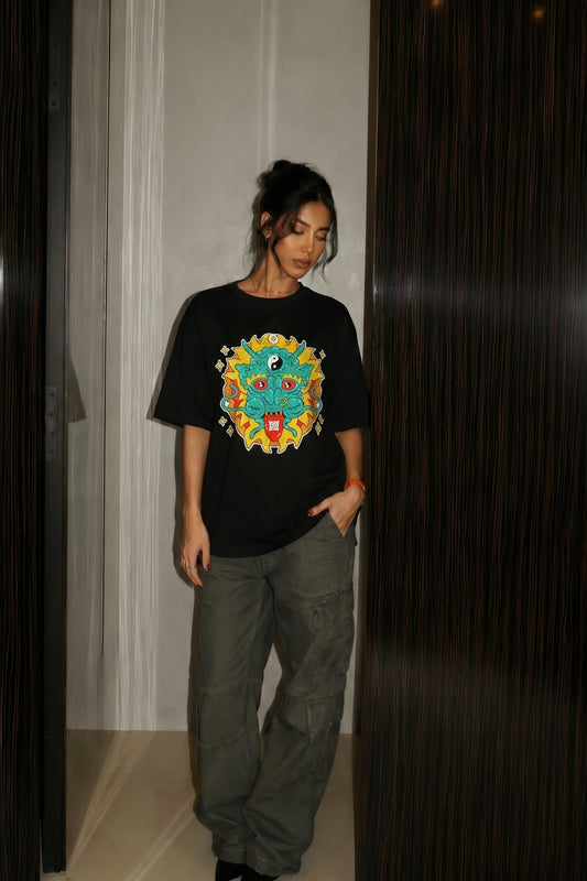Person wearing a black t-shirt with a colorful embroidery design and gray pants indoors.