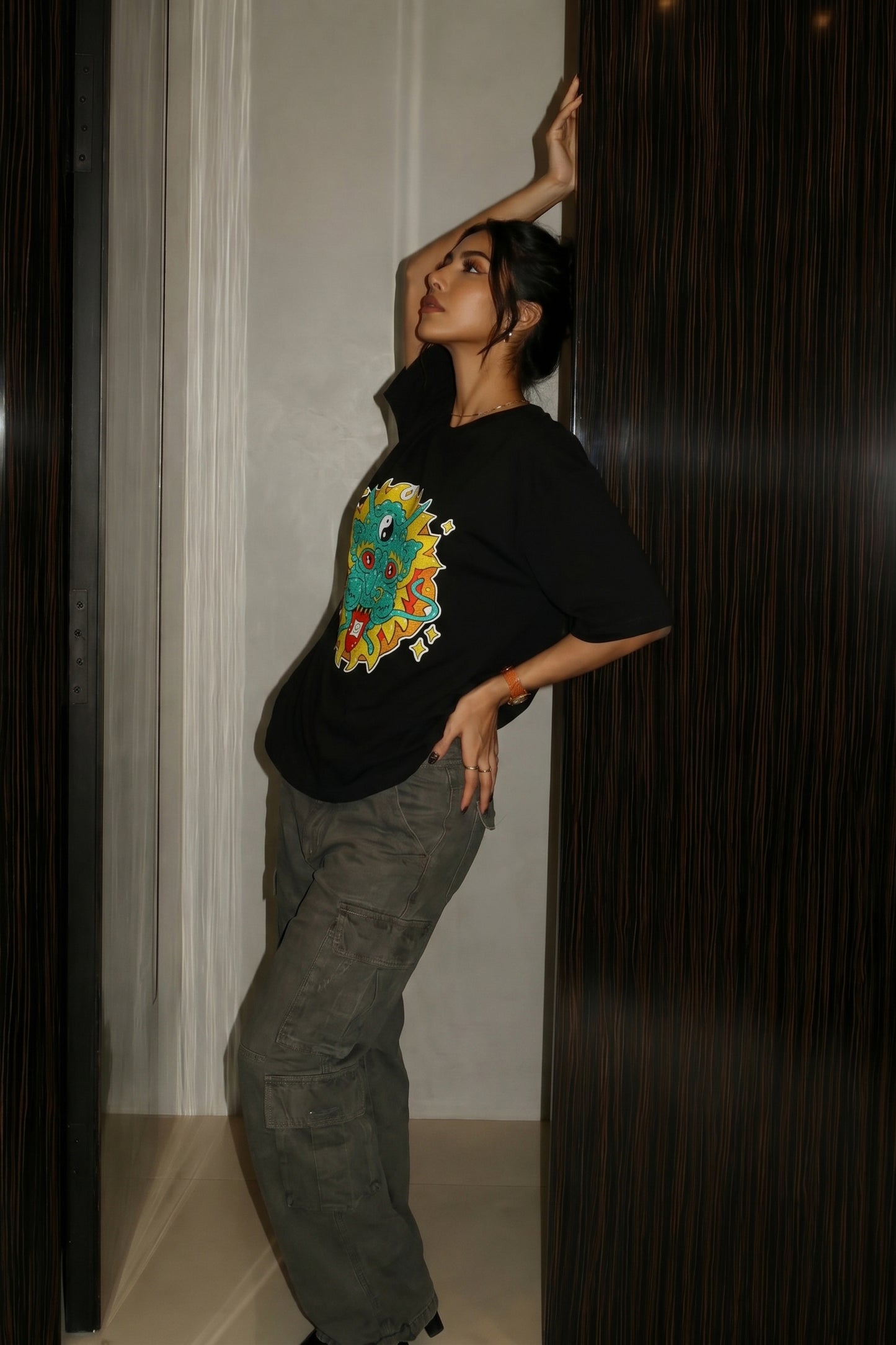 Person wearing a black t-shirt with a colorful embroidery design, standing against a dark background.