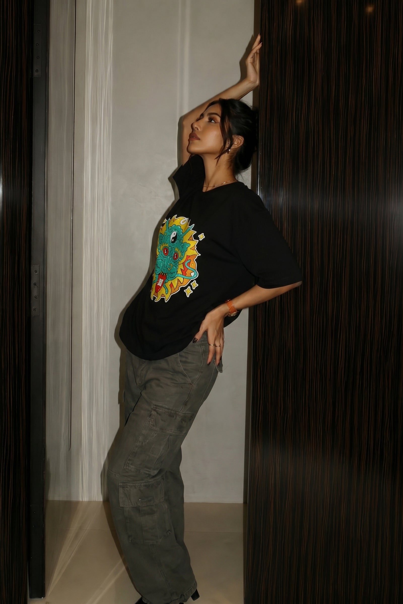 Person wearing a black t-shirt with a colorful embroidery design, standing against a dark background.