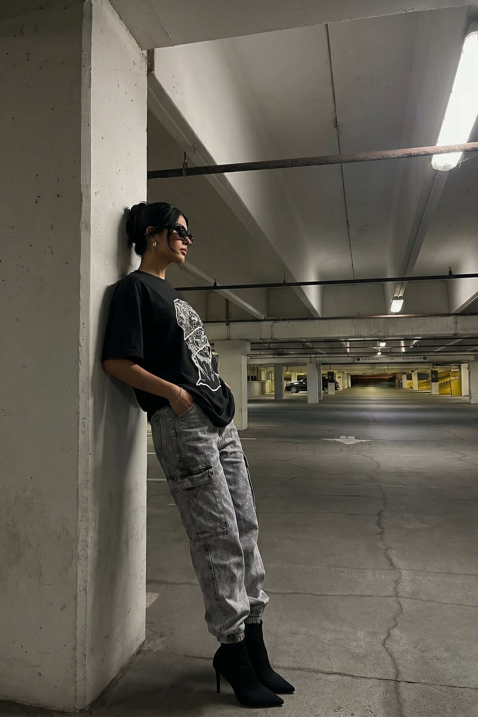 Person wearing a black t-shirt with a embroidery design and gray pants in an underground parking lot.