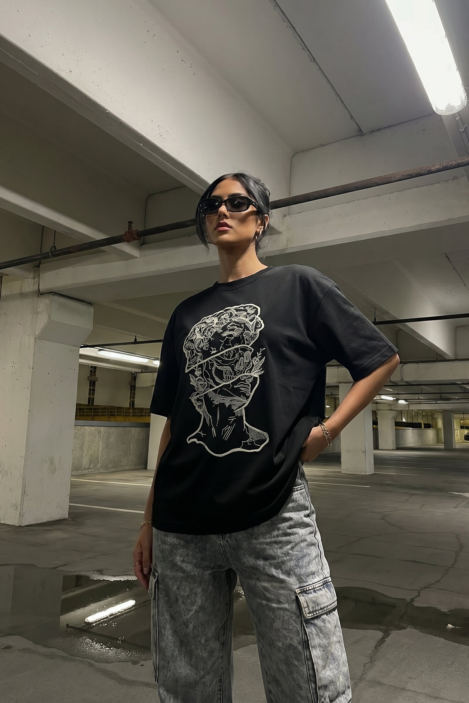 Person wearing a black t-shirt with a embroidery design and gray pants in an underground parking lot.
