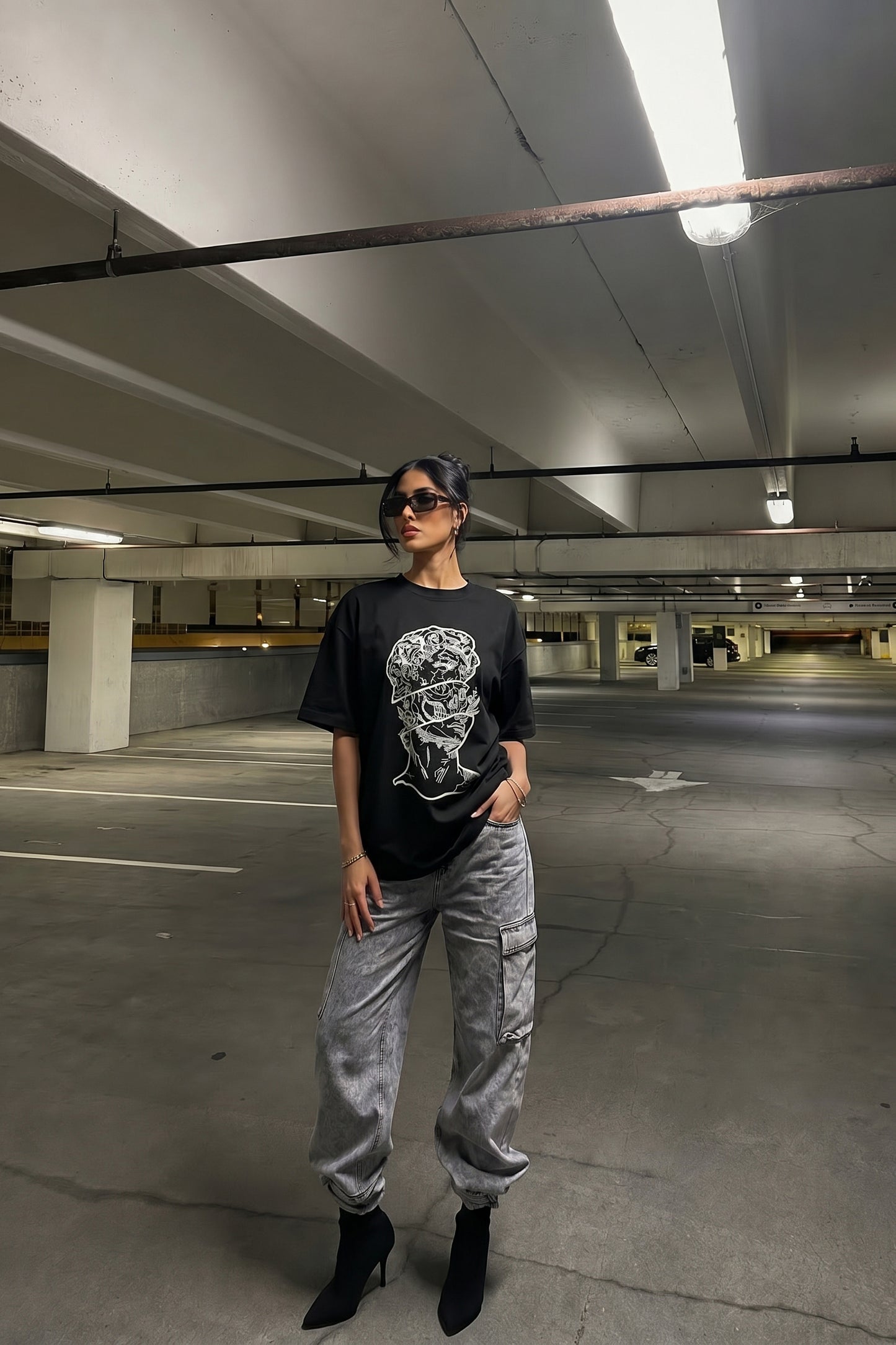 Person wearing a black t-shirt with a embroidery design and gray pants in an underground parking lot.
