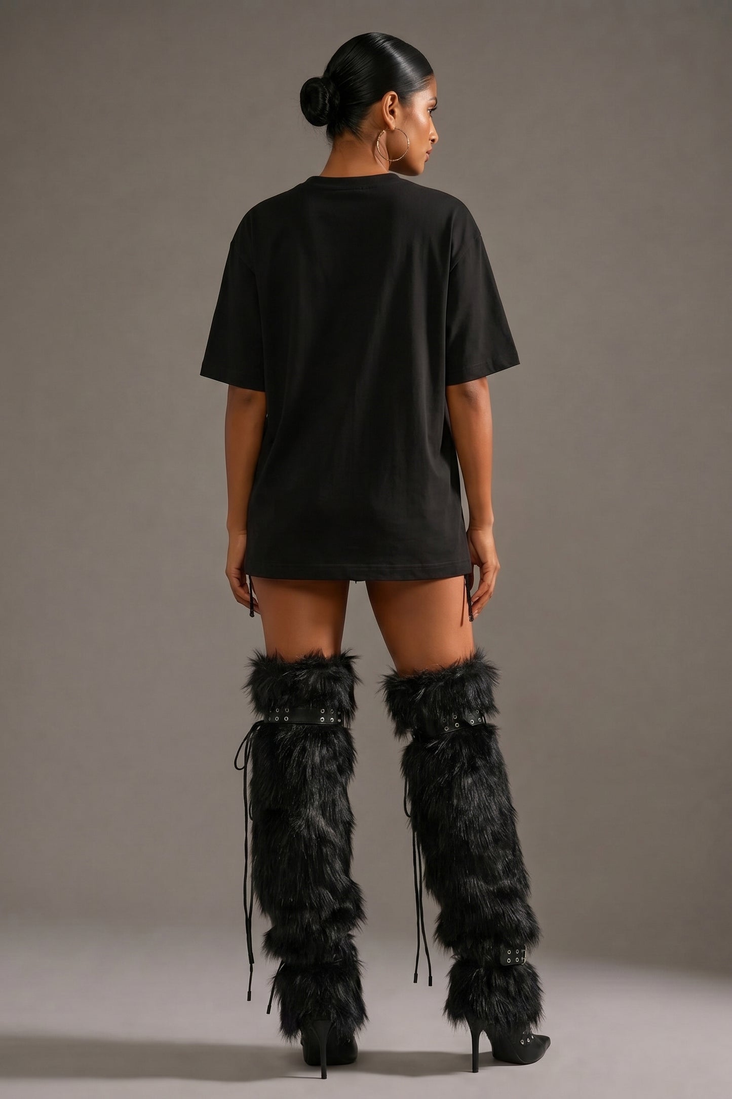 Person wearing a black oversized t-shirt and black feathered high boots on a gray background