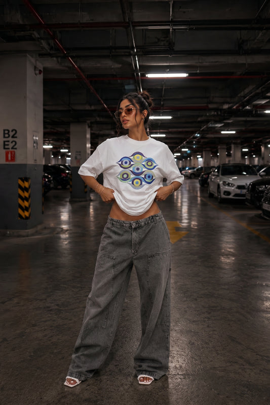 Person wearing a white t-shirt with a colorful embroidery design and gray pants in a parking garage.