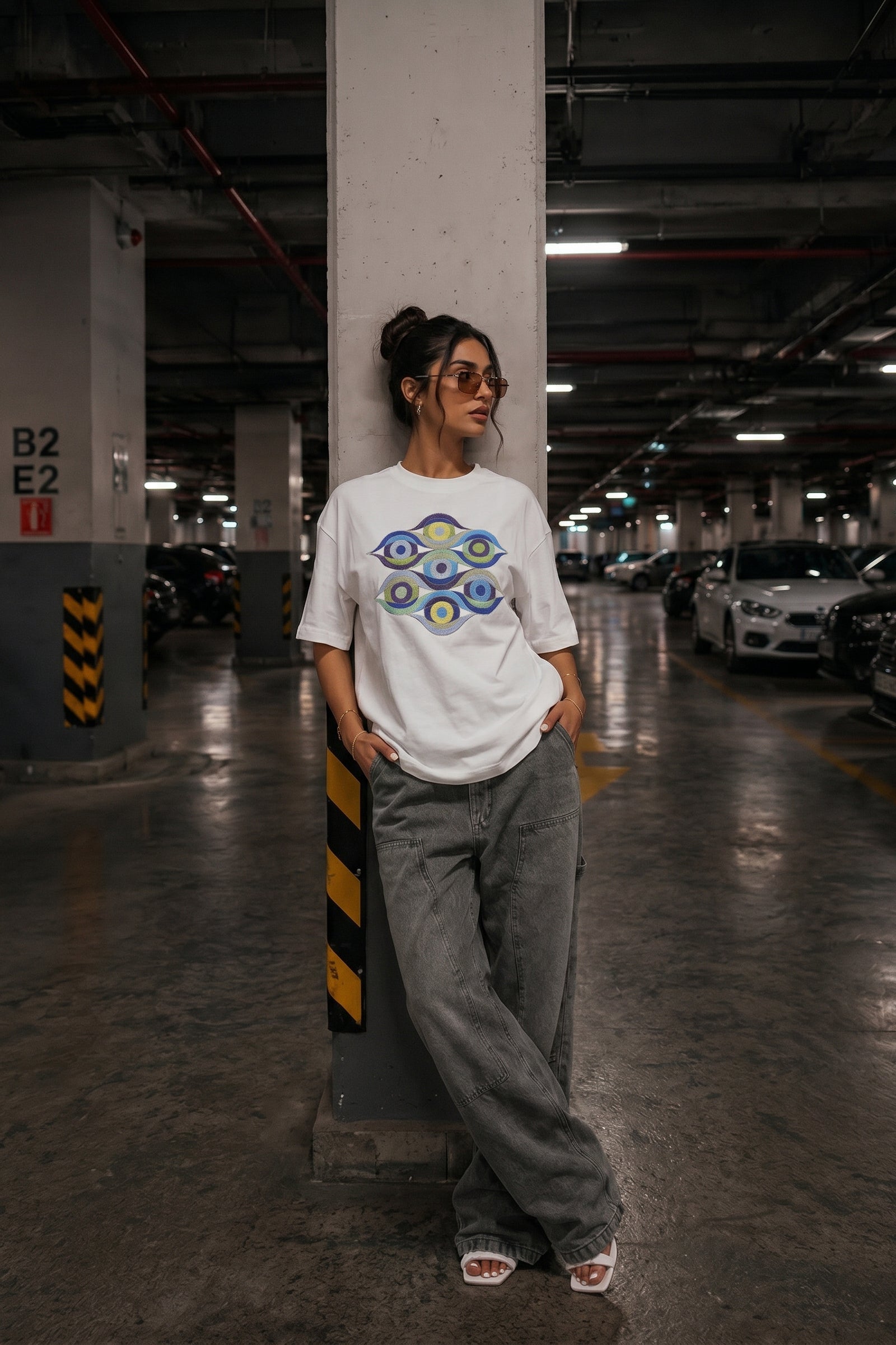 Person wearing a white t-shirt with a colorful embroidery design and gray pants in a parking garage.