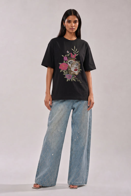 Woman wearing a black t-shirt with floral and butterfly embroidery design and blue jeans on a white background
