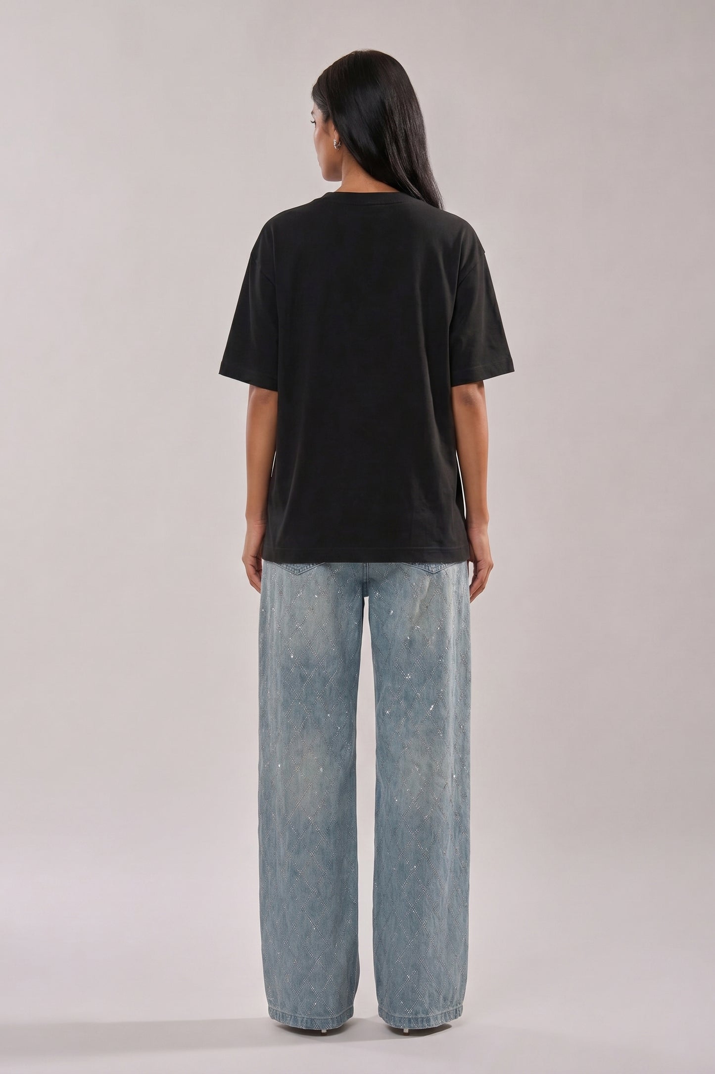 Woman wearing a black t-shirt with floral and butterfly embroidery design and blue jeans on a white background
