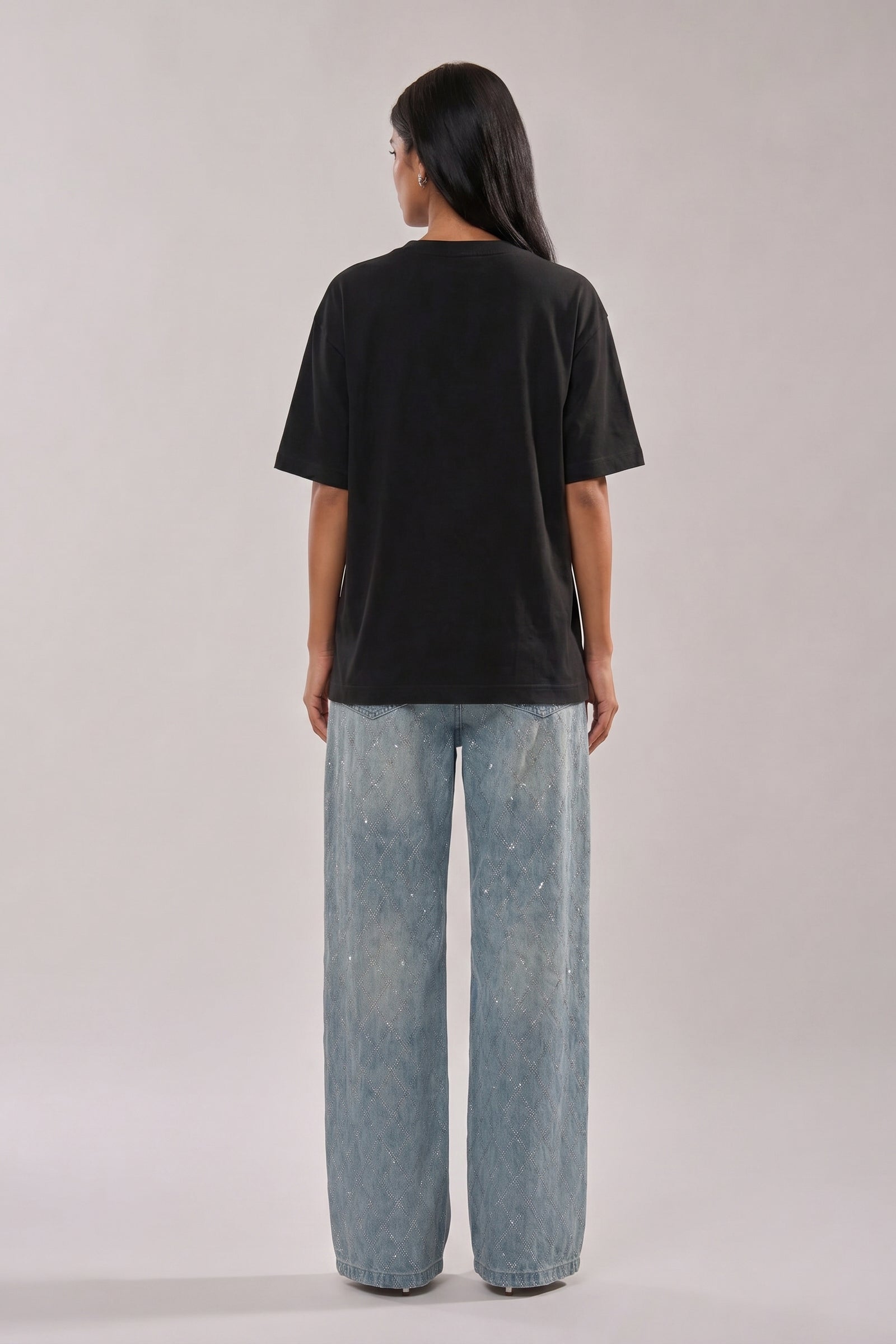 Woman wearing a black t-shirt with floral and butterfly embroidery design and blue jeans on a white background