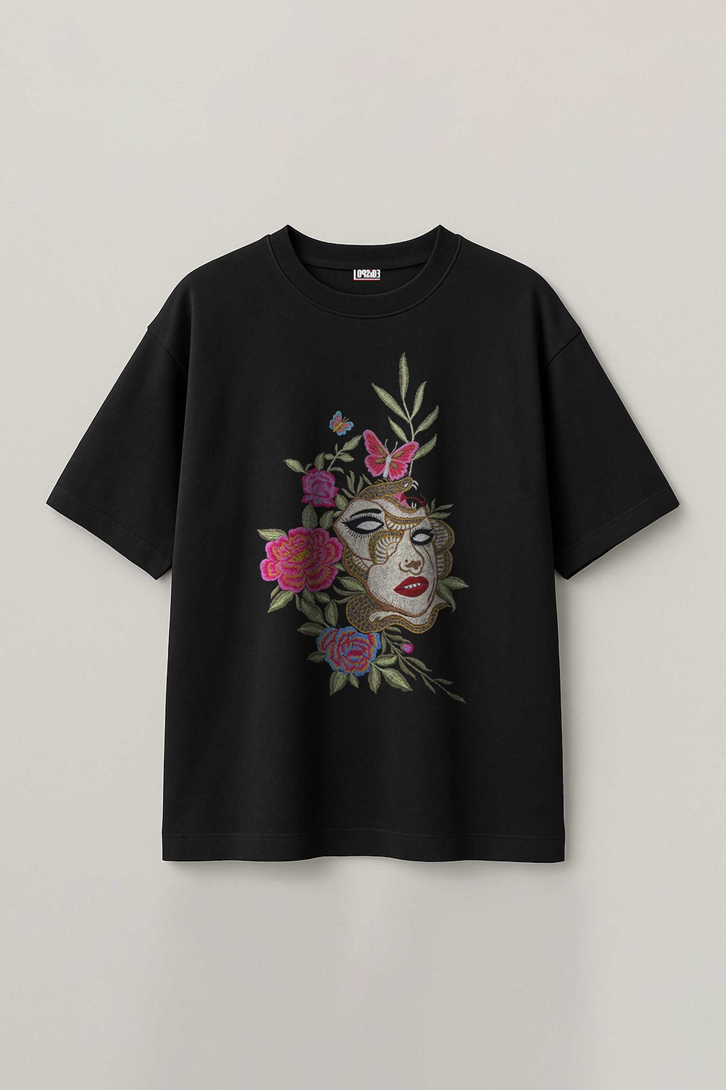 Black t-shirt with embroidered face and floral embroidery design on a light gray background