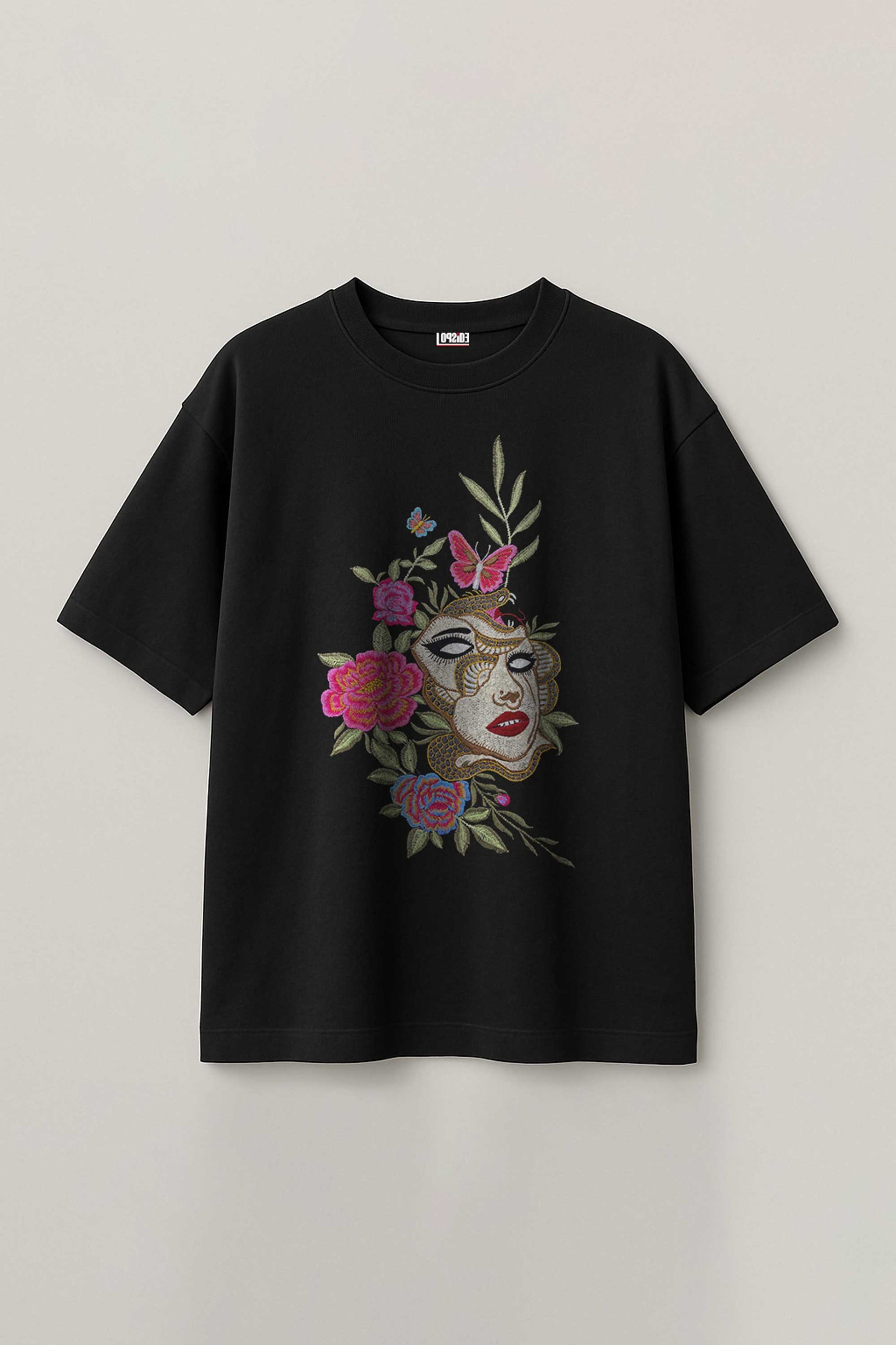 Black t-shirt with embroidered face and floral embroidery design on a light gray background
