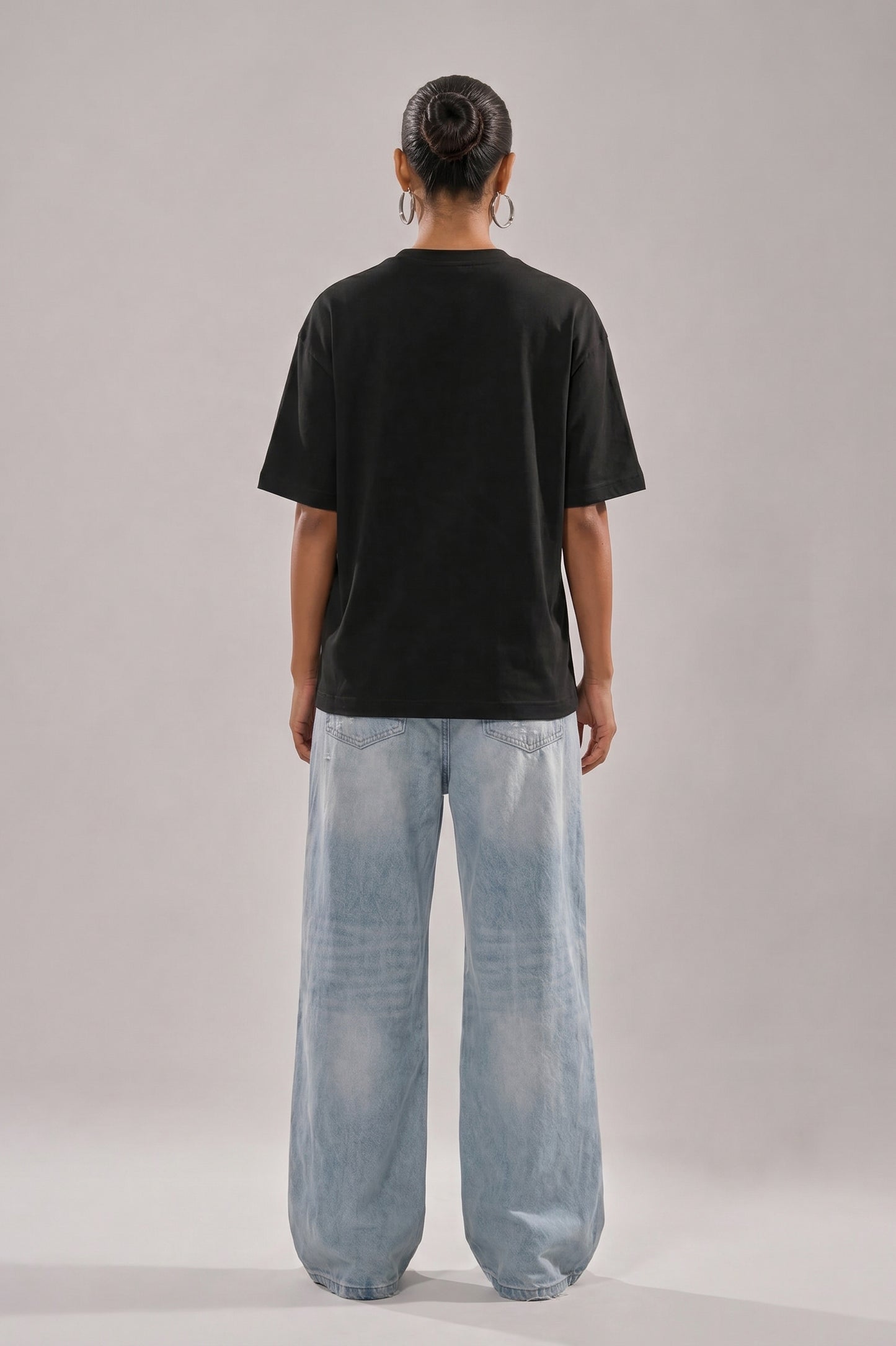 Person wearing a black t-shirt and light blue jeans on a plain background
