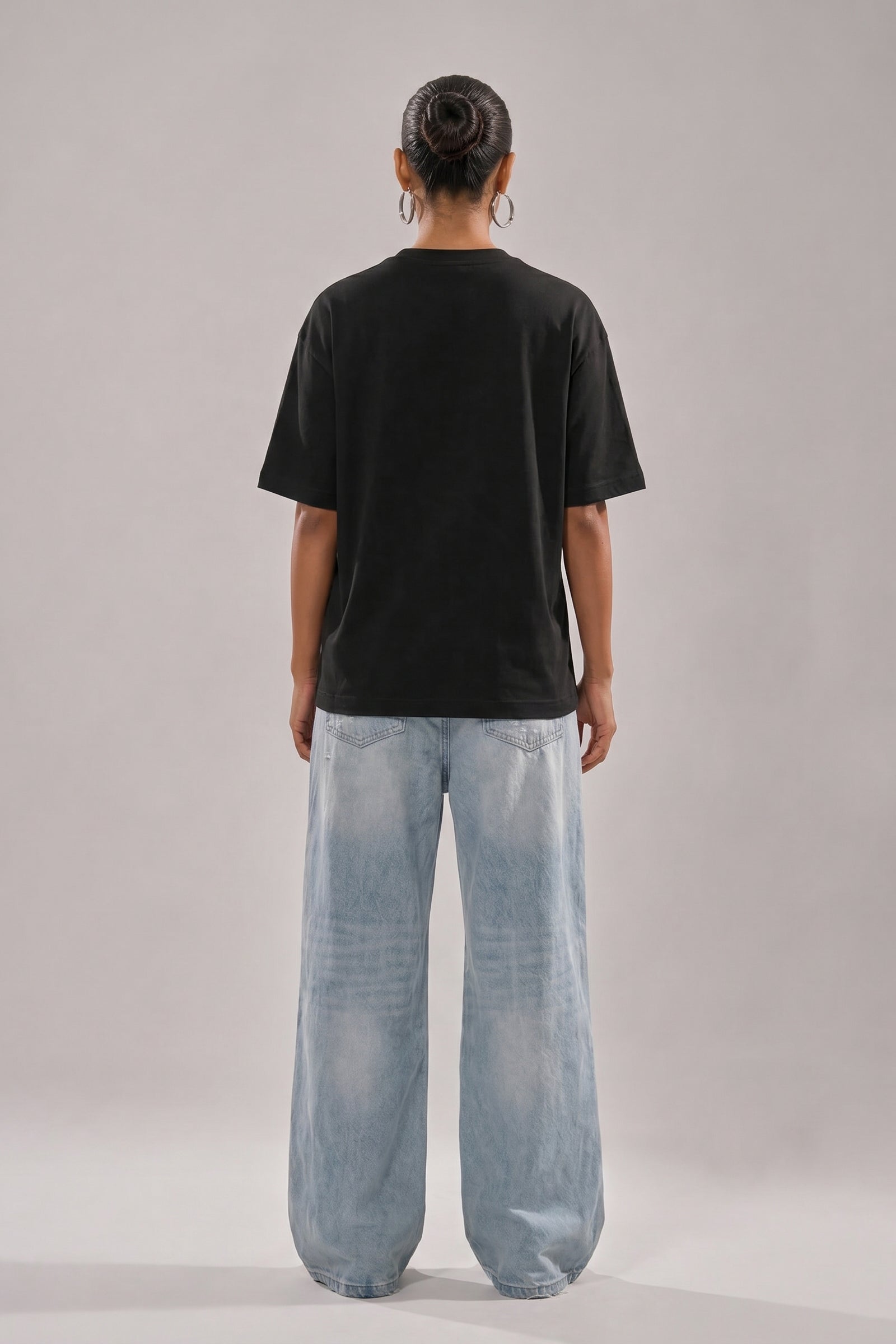 Person wearing a black t-shirt and light blue jeans on a plain background