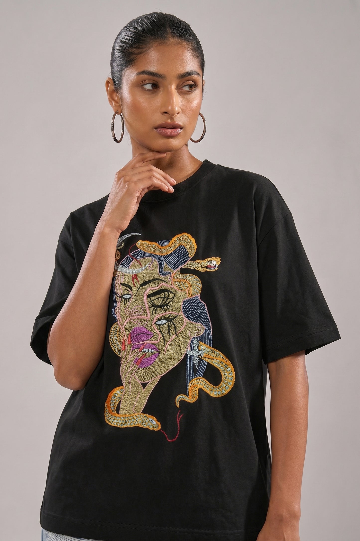 Person wearing a black t-shirt with a embroidery design and light blue jeans on a plain background