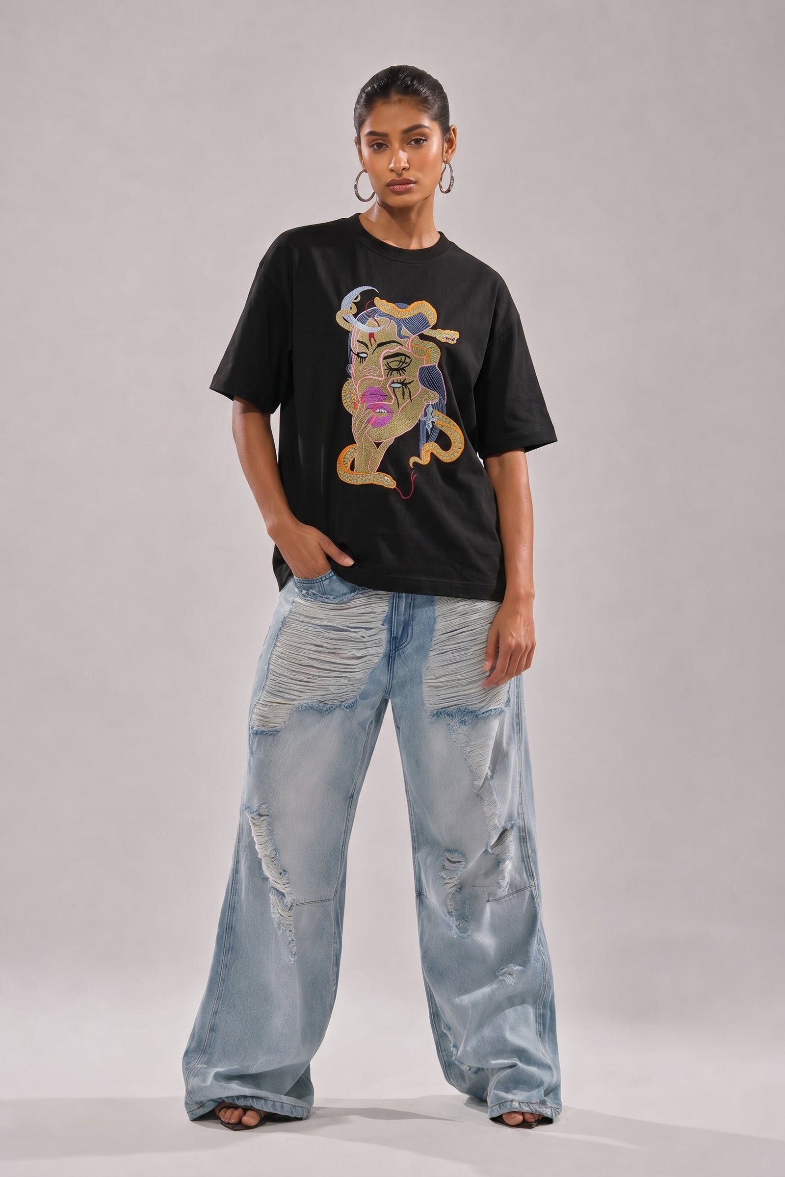 Person wearing a black t-shirt with a embroidery design and light blue jeans on a plain background