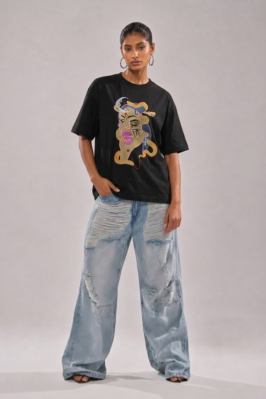 Person wearing a black t-shirt with a embroidery design and light blue jeans on a plain background