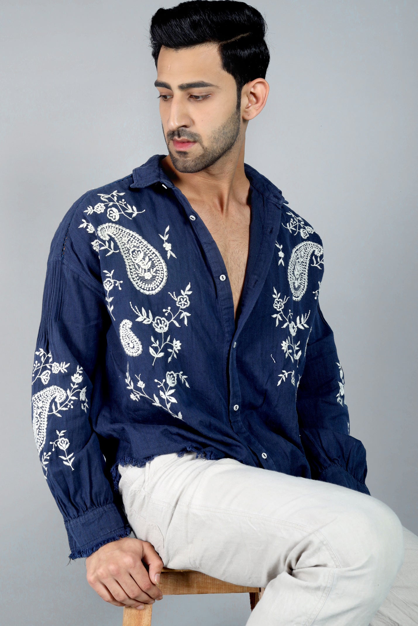 Man wearing a navy blue embroidered shirt with white patterns on a gray background
