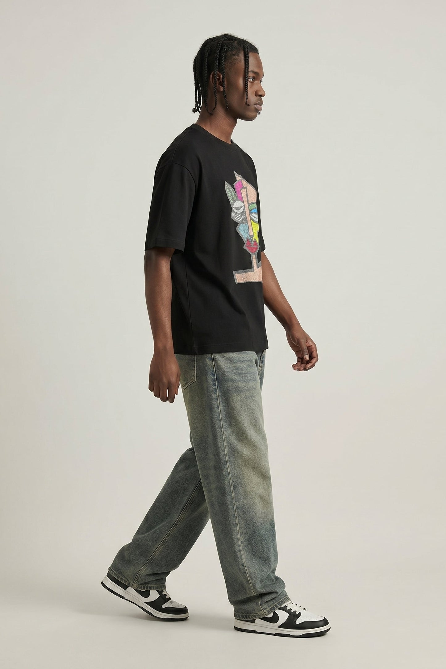 Person wearing a black t-shirt with a colorful graphic and light blue jeans on a plain background