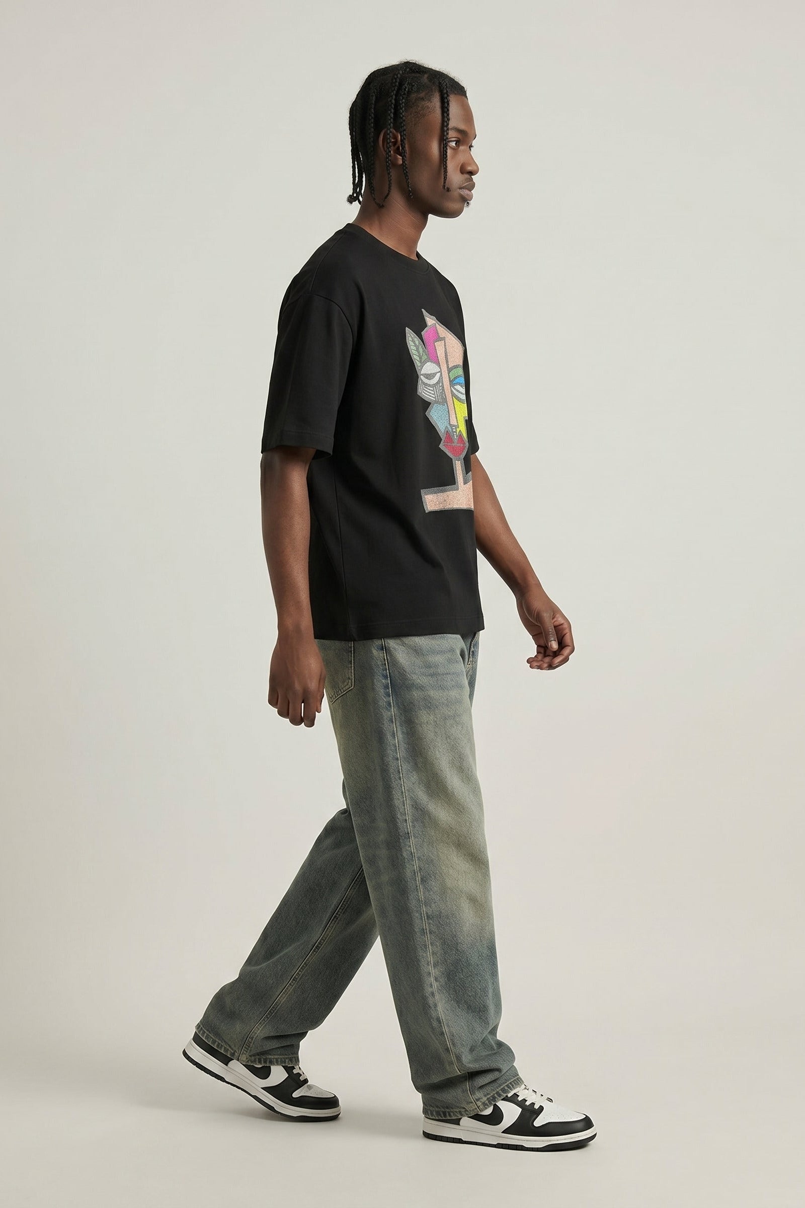 Person wearing a black t-shirt with a colorful graphic and light blue jeans on a plain background