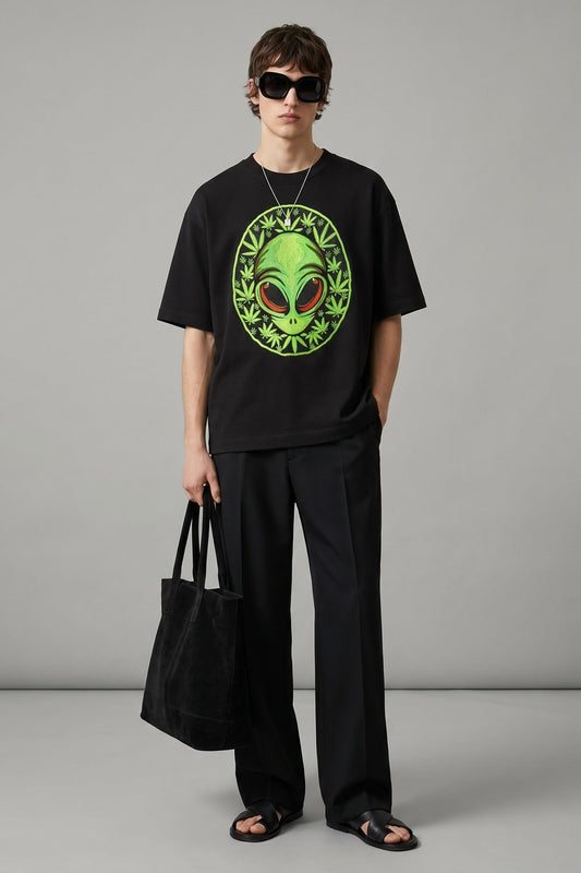 Person wearing a black t-shirt with an alien graphic and holding a black bag on a gray background