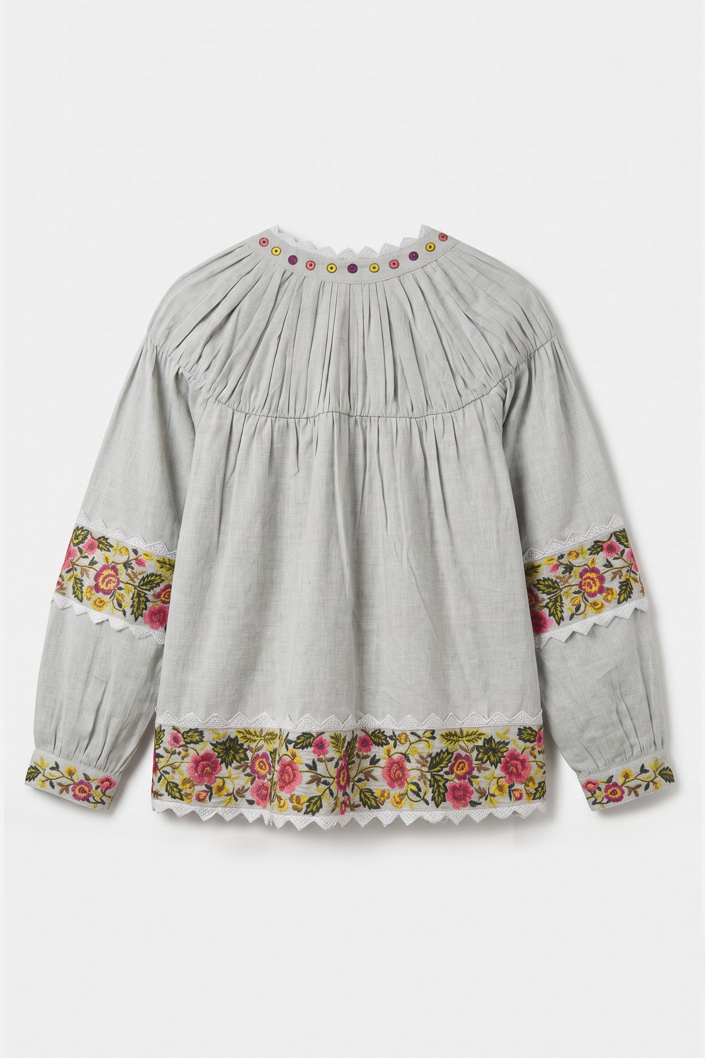 A light gray long-sleeve blouse with a pleated bodice, floral embroidered cuffs, and a matching floral hem, shown against a plain light gray background.