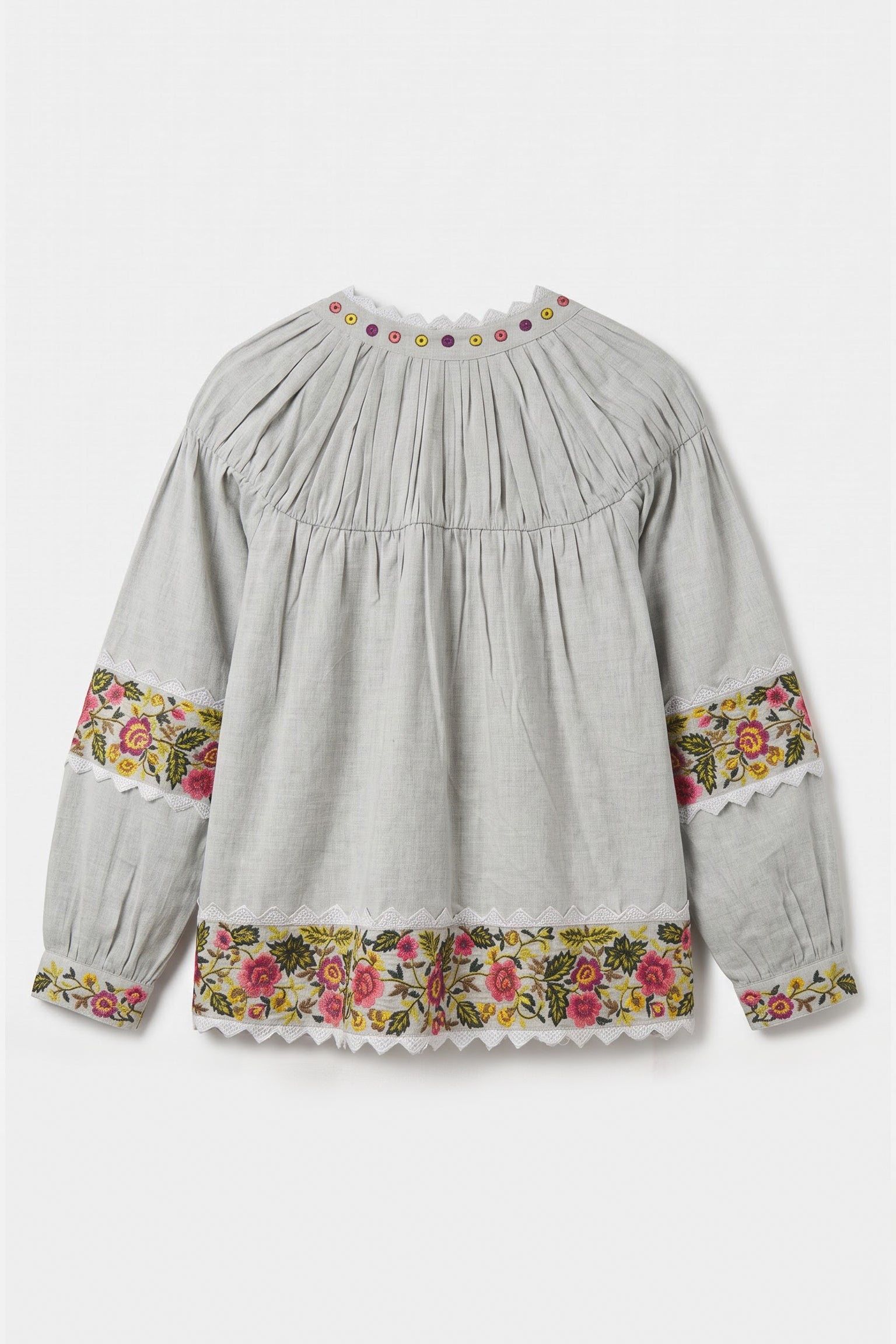 A light gray long-sleeve blouse with a pleated bodice, floral embroidered cuffs, and a matching floral hem, shown against a plain light gray background.
