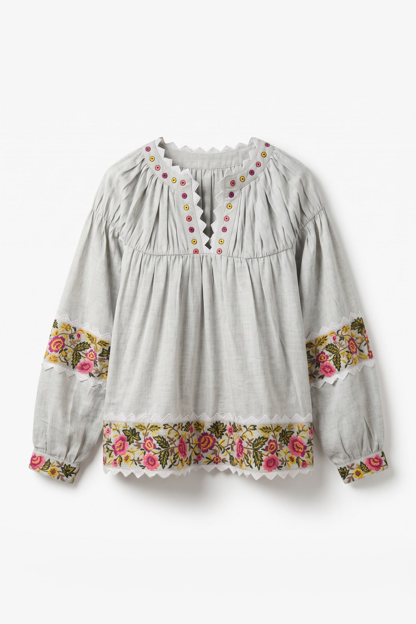 A light gray long-sleeve blouse with a gathered smocked bodice, scalloped neckline, and floral embroidered trim on the cuffs and hem.