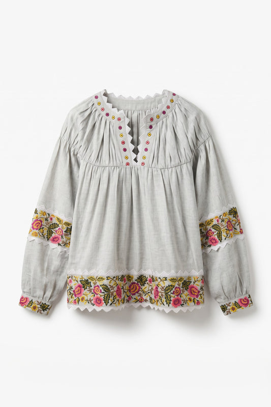 A light gray long-sleeve blouse with a gathered smocked bodice, scalloped neckline, and floral embroidered trim on the cuffs and hem.