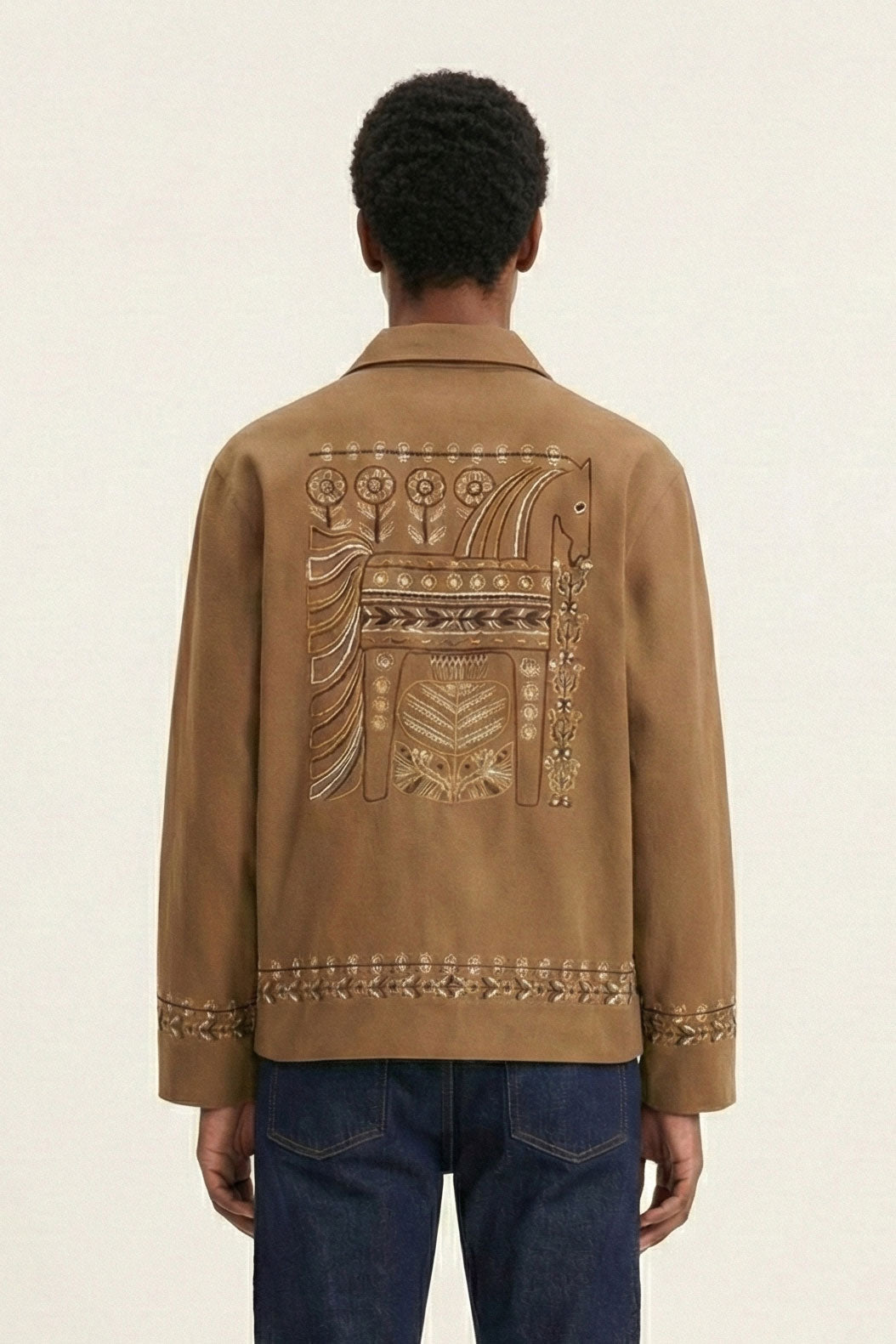 Person wearing a brown jacket with intricate designs on the back against a beige background