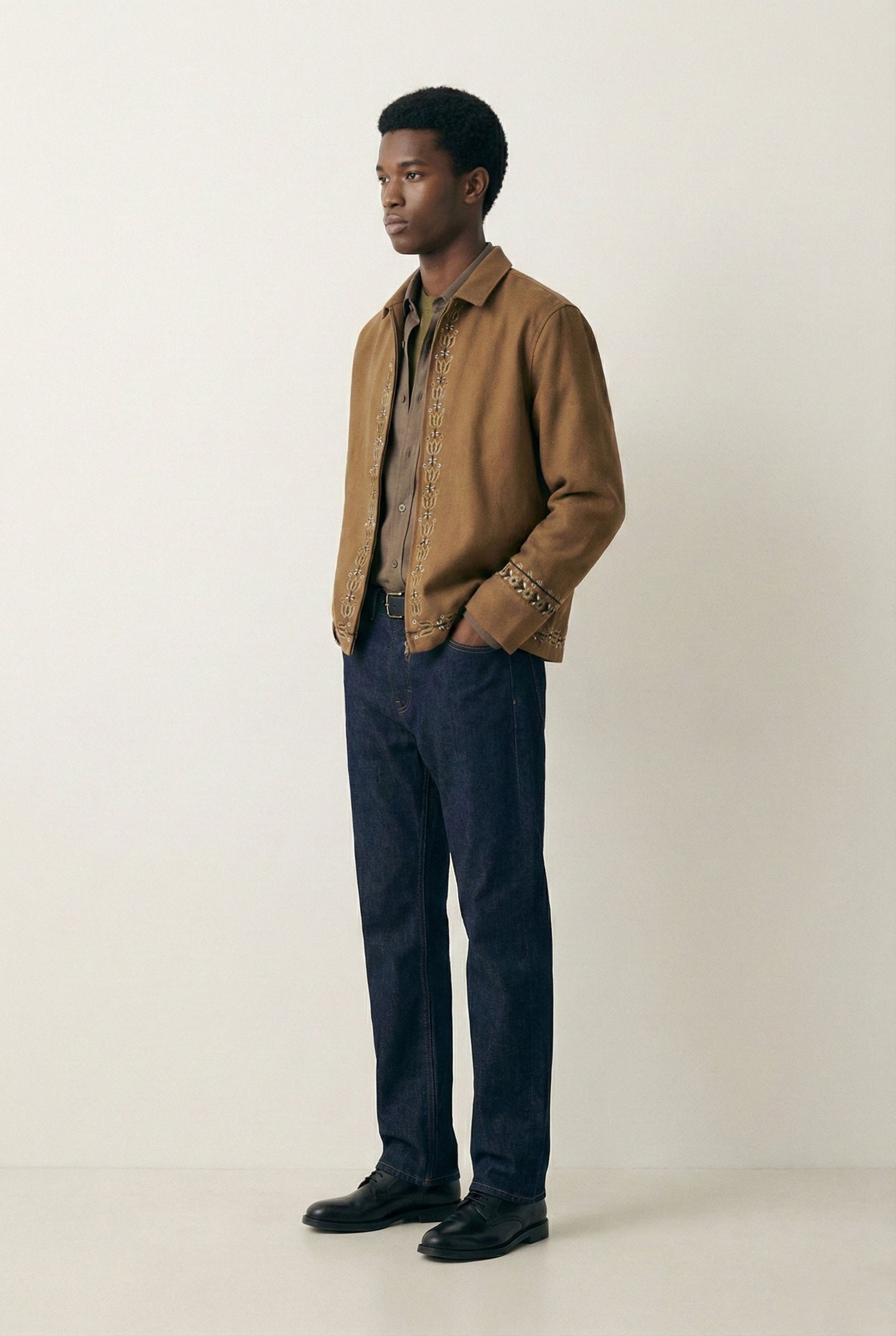 Man wearing a brown jacket and dark pants on a white background