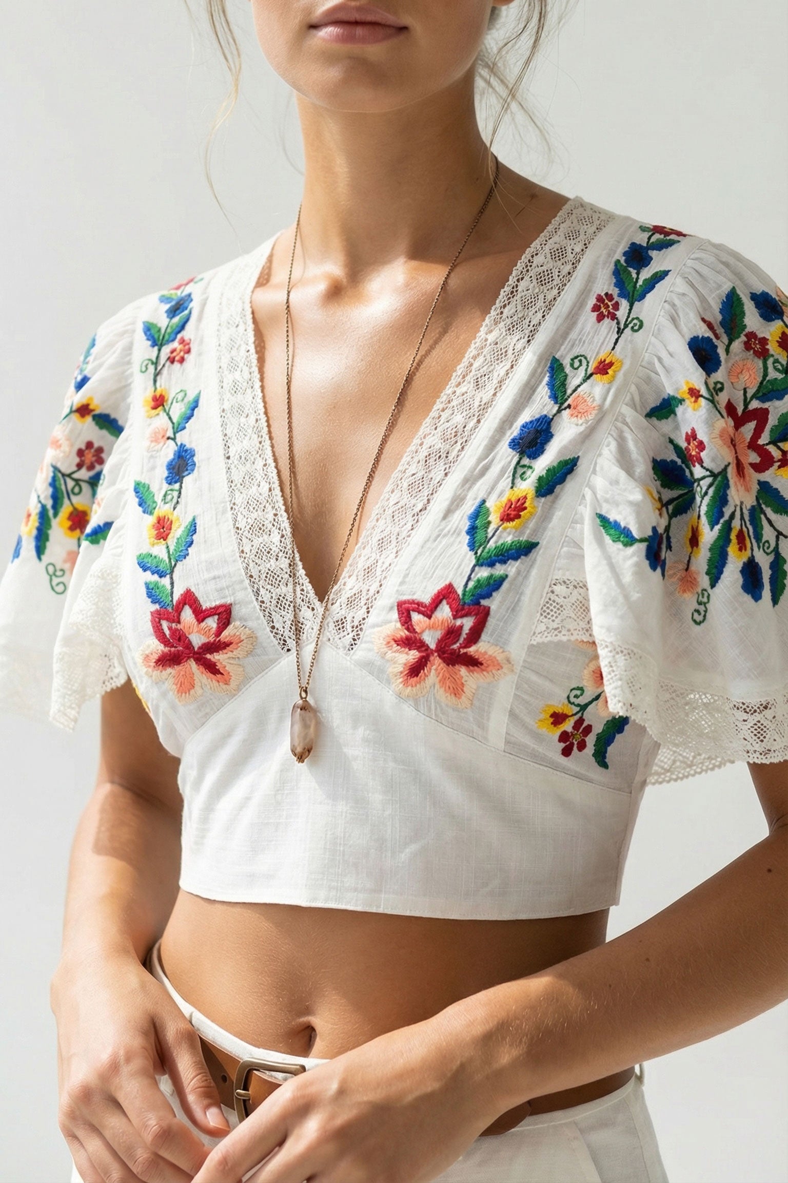 White lace top with colorful floral embroidery on a plain background