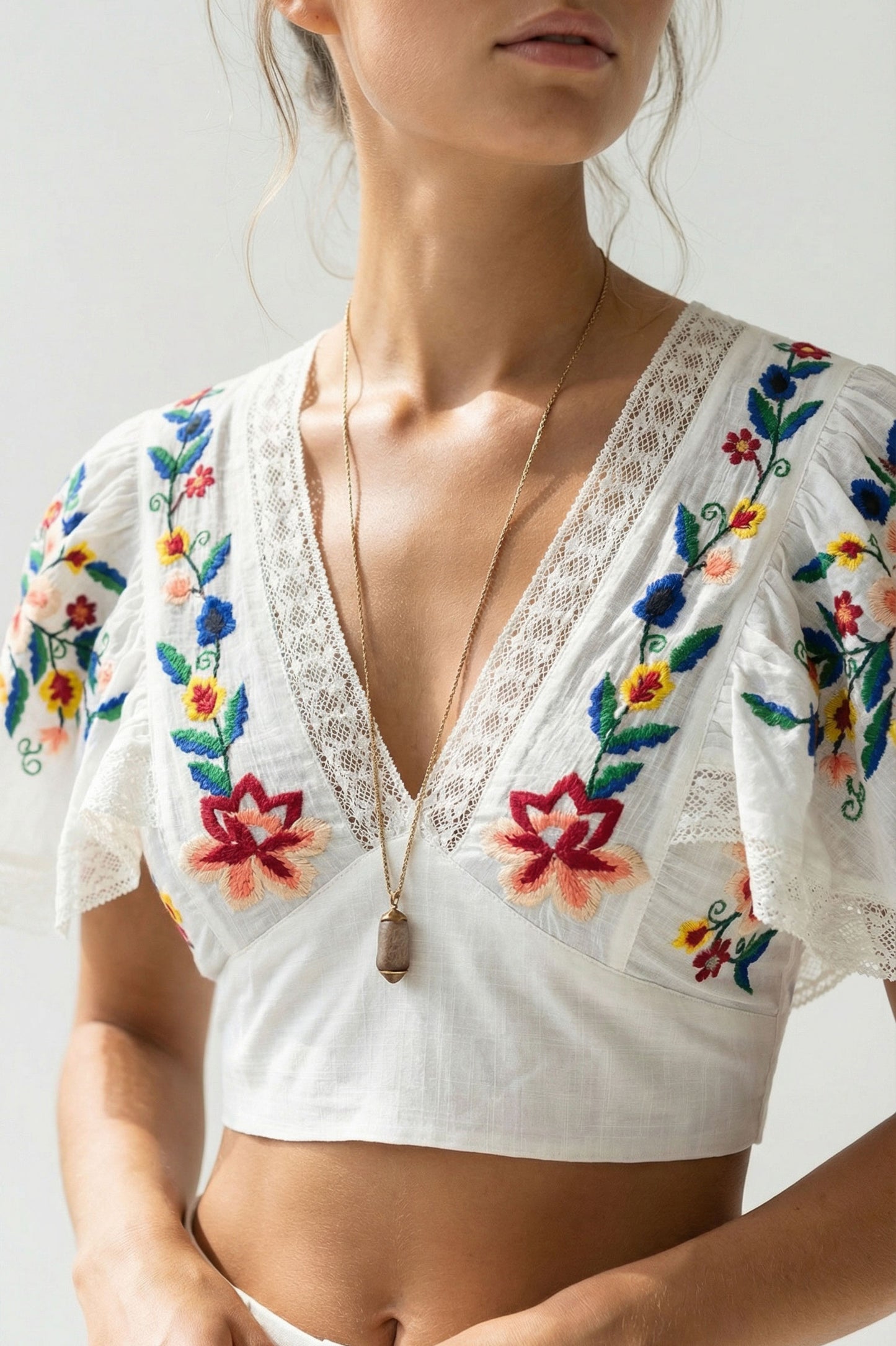 White embroidered top with colorful floral patterns on a plain background