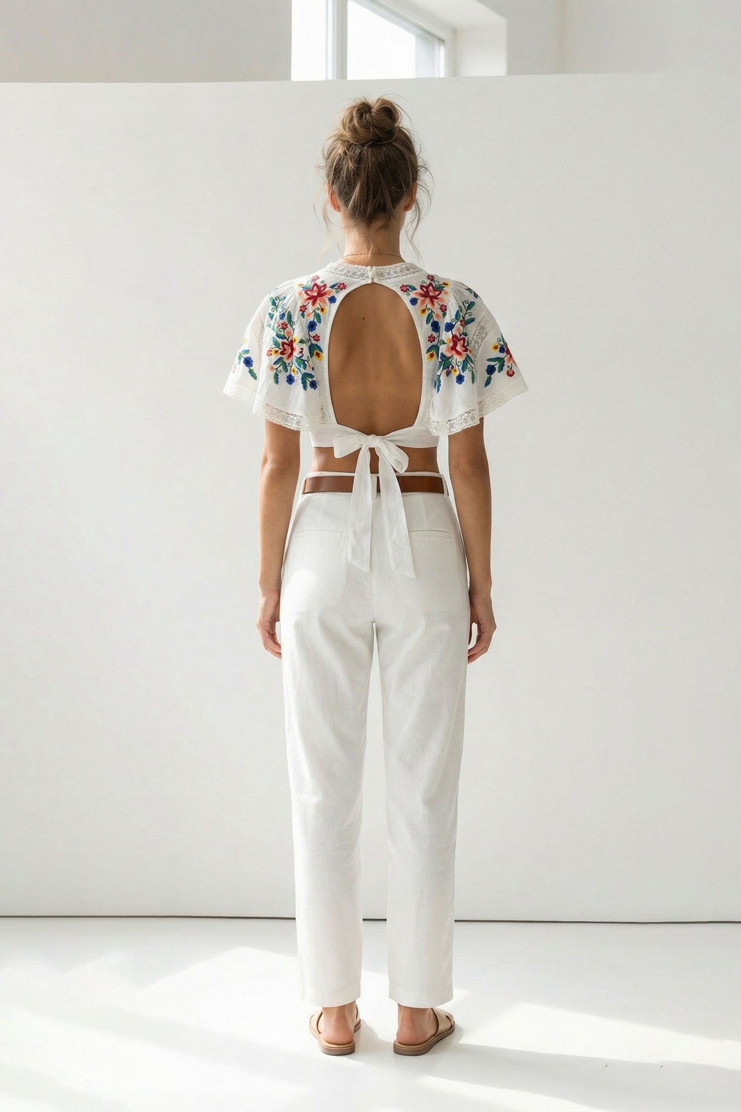 Woman wearing a white outfit with floral embroidery on the back against a white background