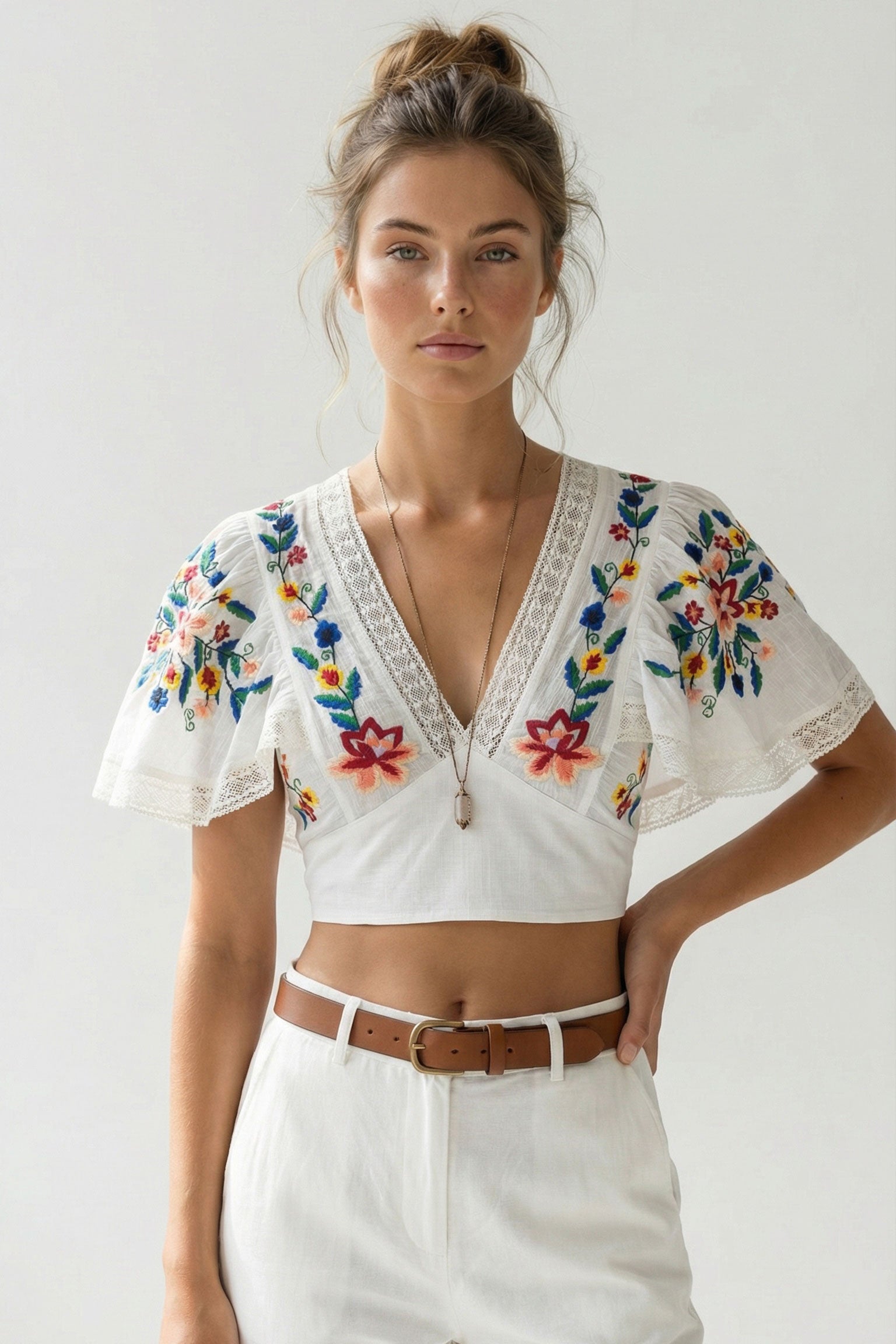 Woman wearing a white blouse with colorful floral embroidery on a plain background
