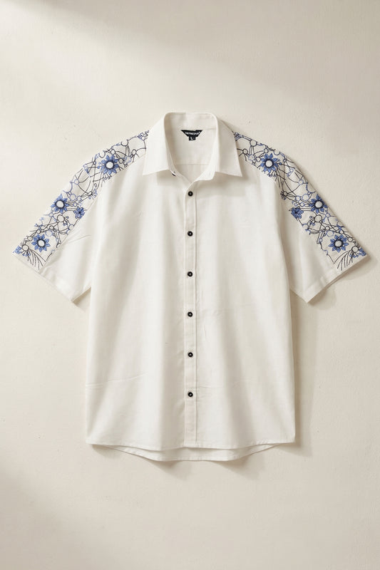 White shirt with blue floral embroidery on sleeves against a beige background