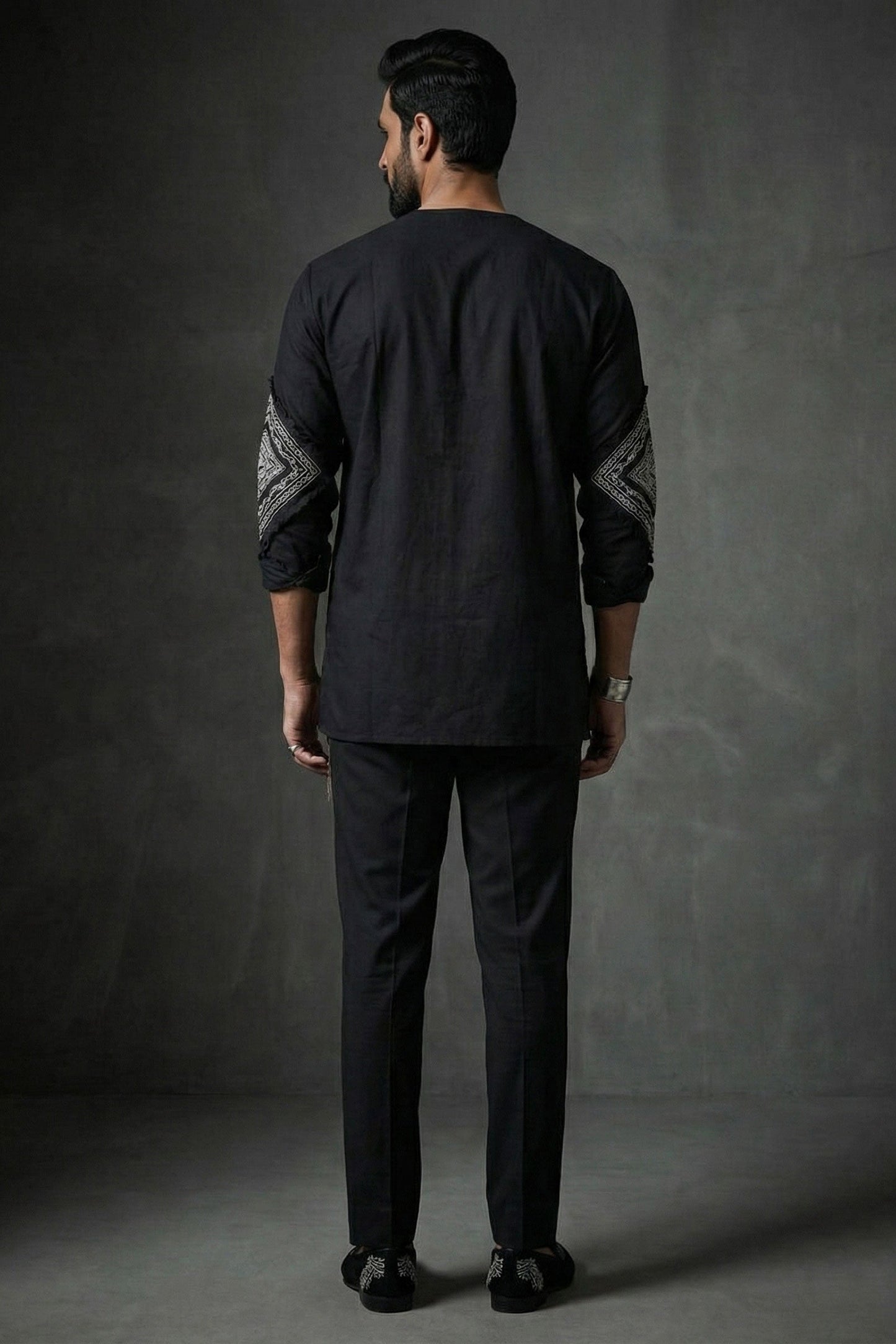 Man wearing a black traditional outfit with patterned sleeves against a dark background