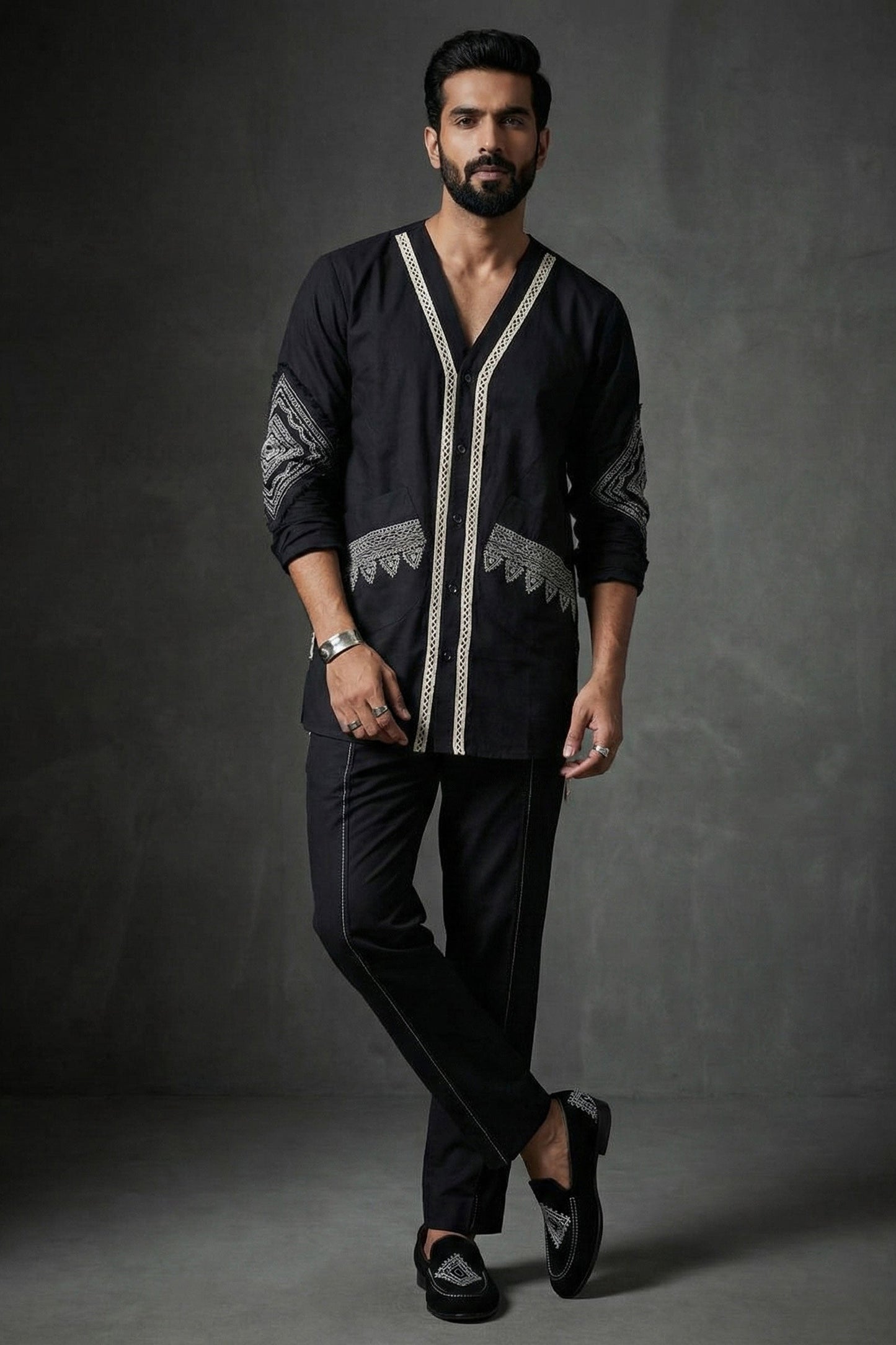 Man wearing a black embroidered shirt and pants against a dark background