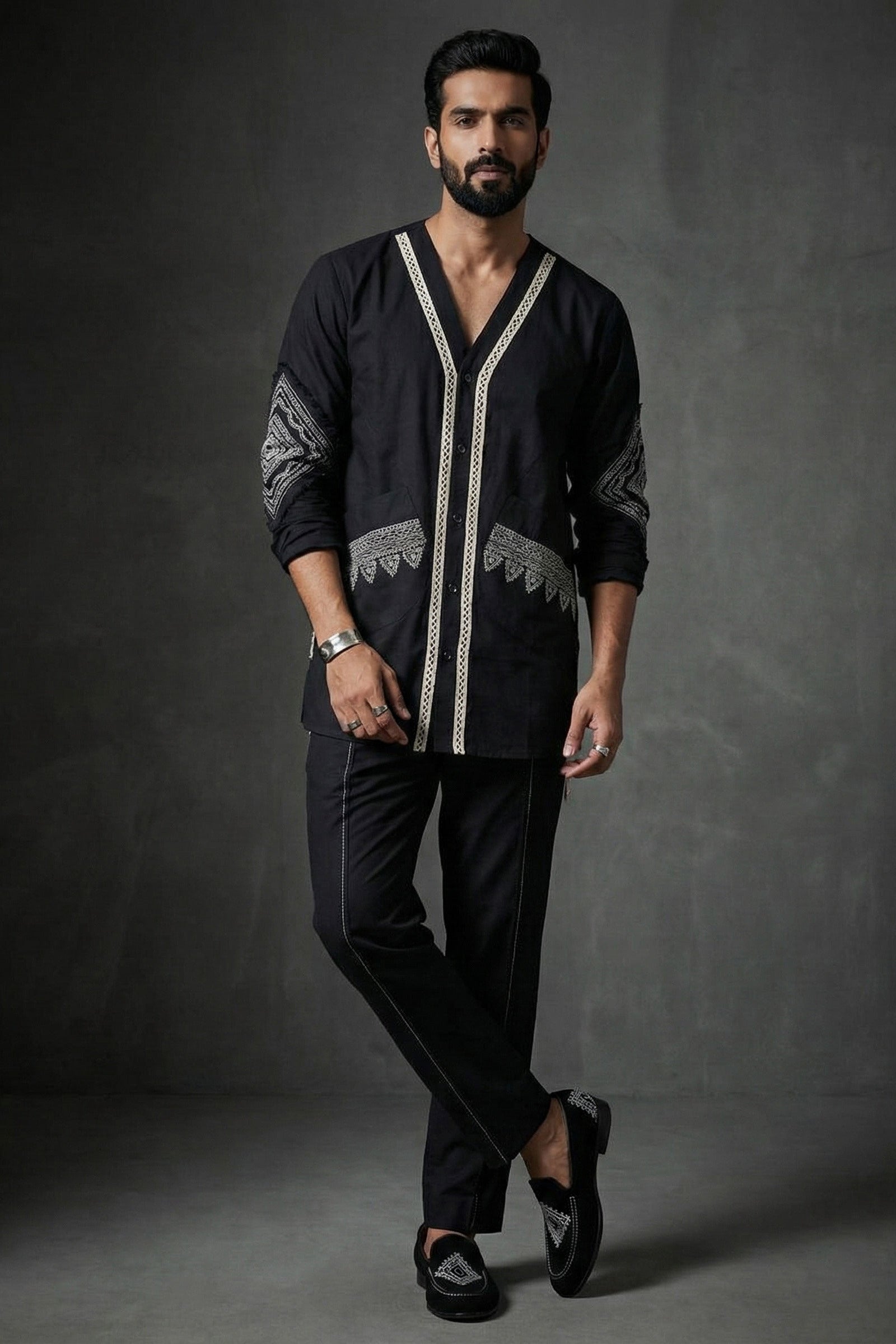 Man wearing a black embroidered shirt and pants against a dark background